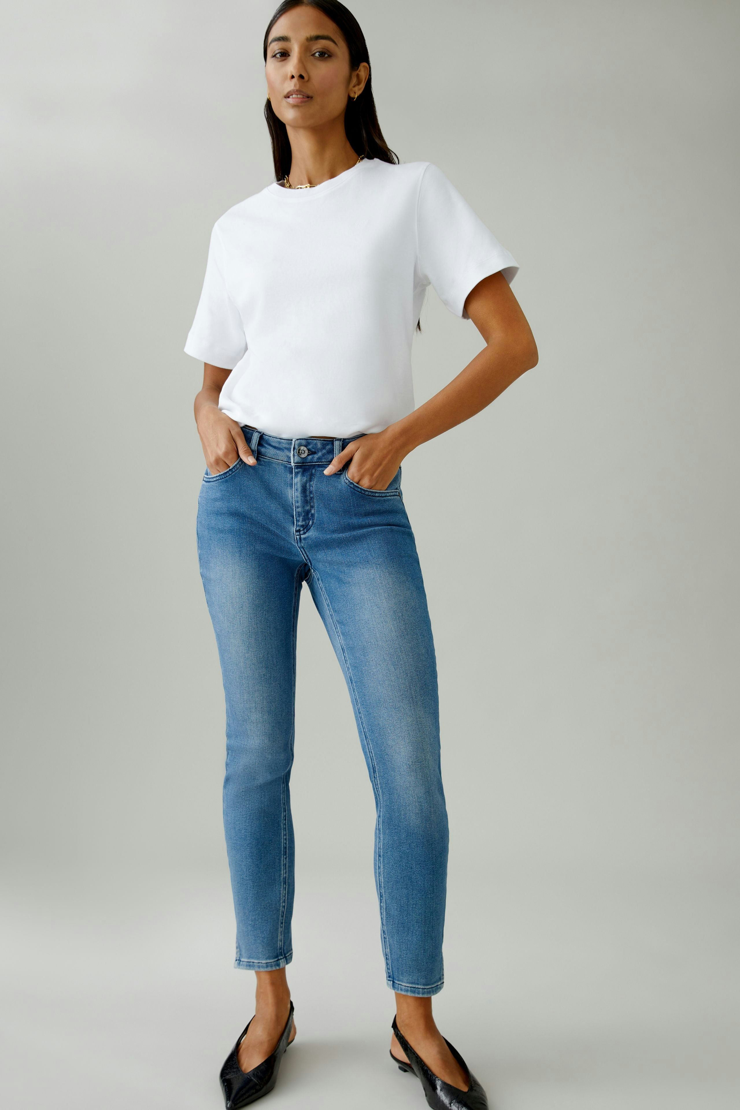 Damen Jeans Skinny: Frau in blauen Skinny Jeans und weißem T-Shirt steht selbstbewusst.