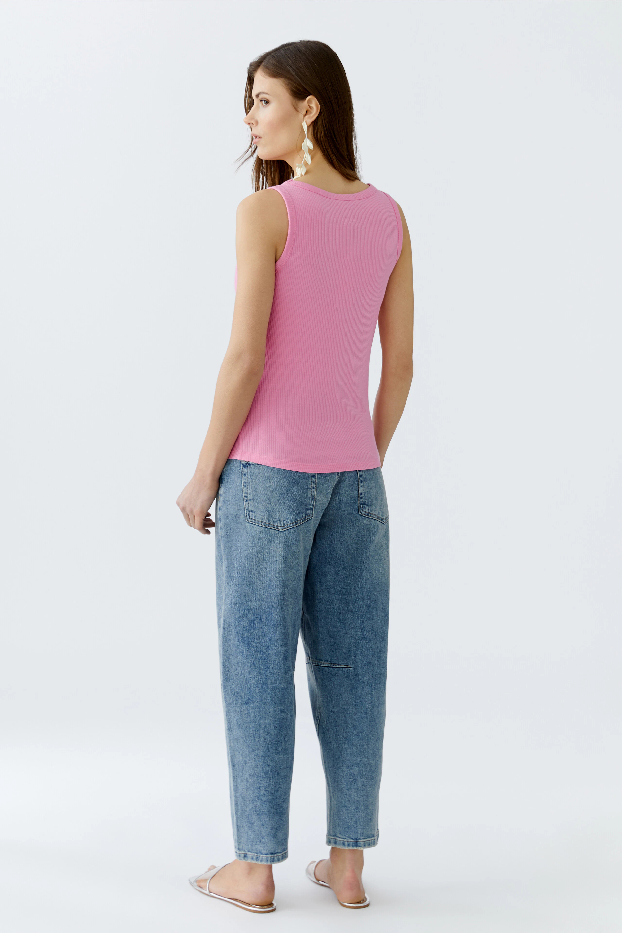 Damen-Top: Frau trägt ein pinkes, ärmelloses Top mit lässigen Jeans und Sandalen.