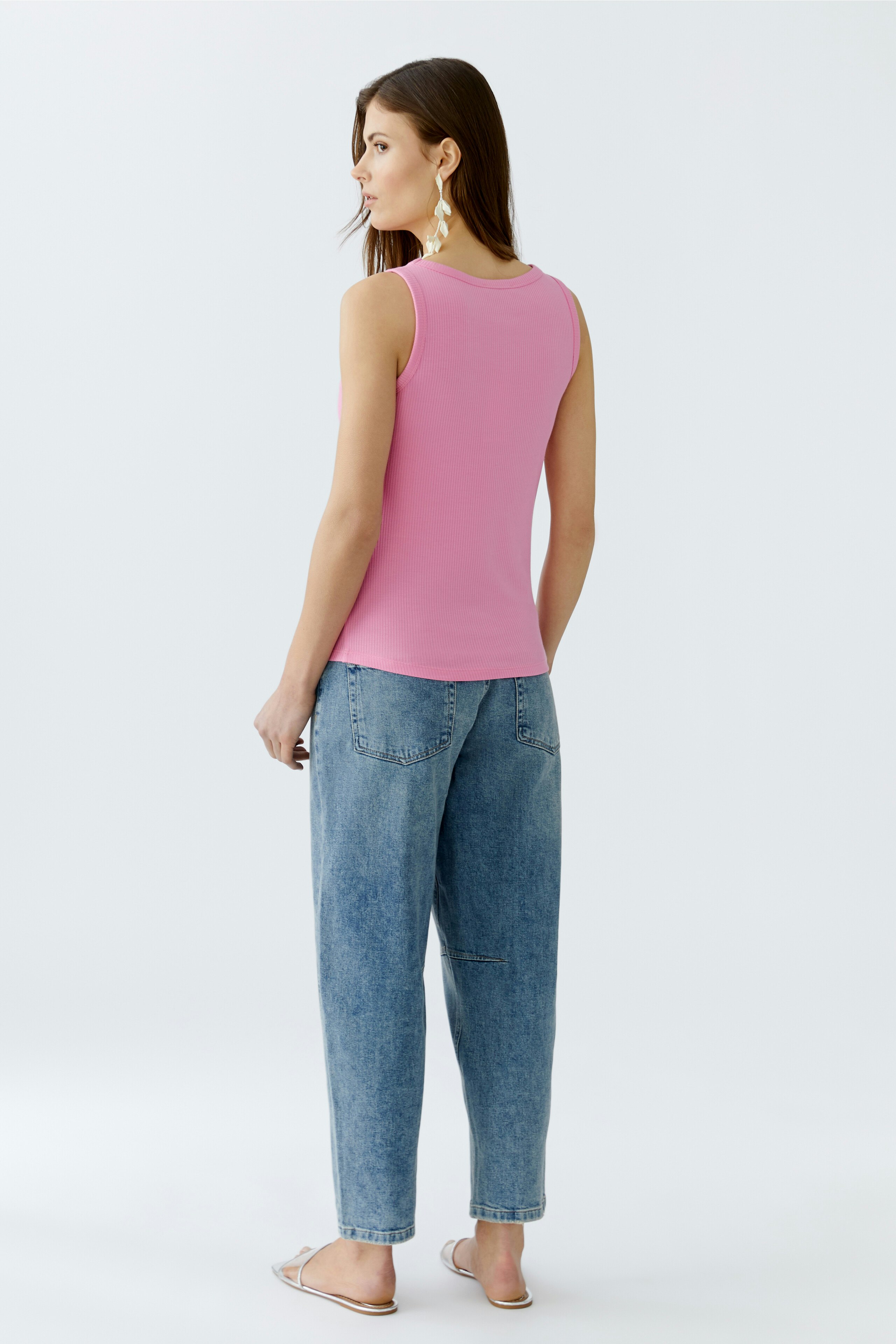 Damen-Top: Frau trägt ein pinkes, ärmelloses Top mit lässigen Jeans und Sandalen.