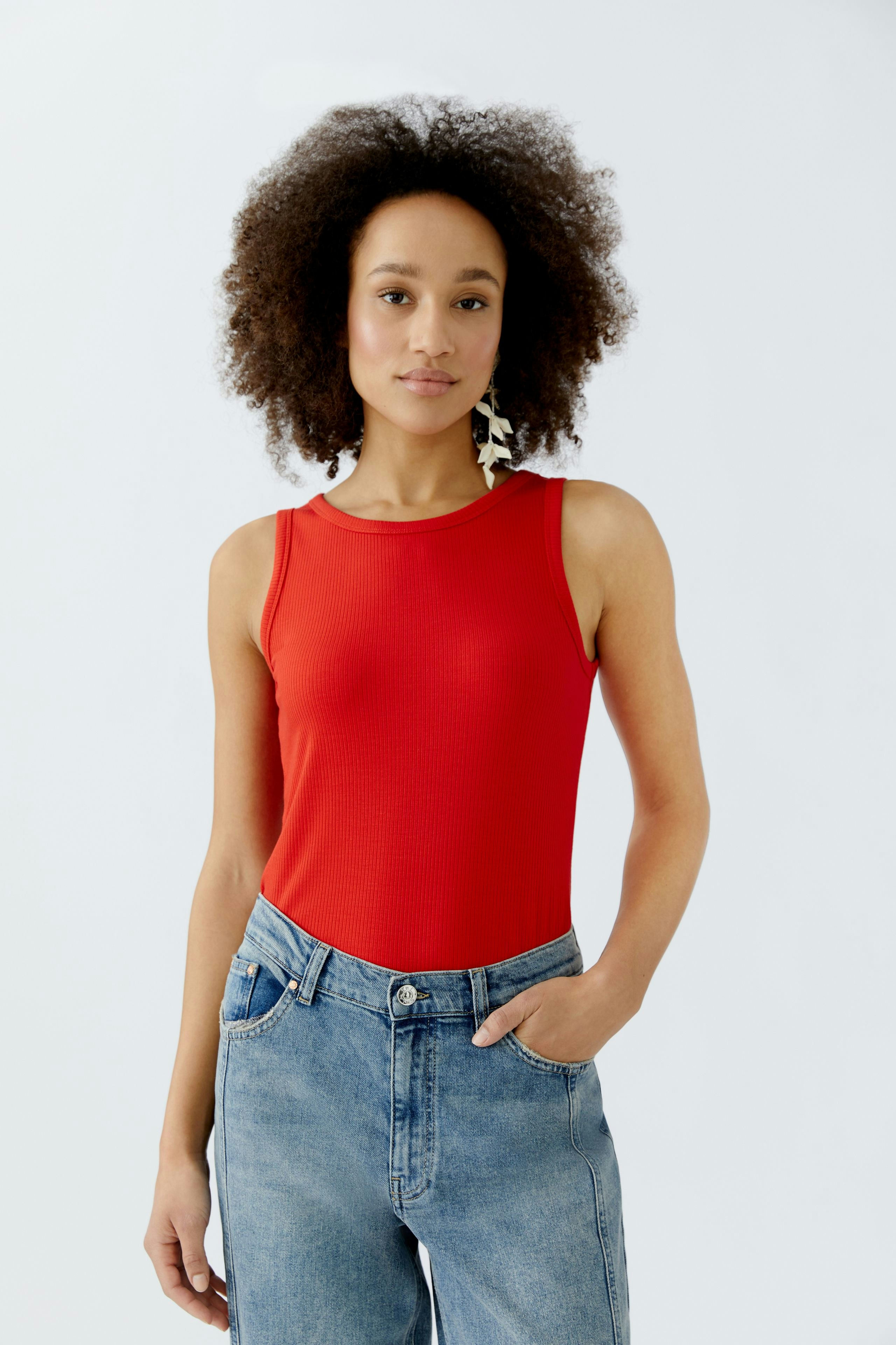 Casual women's top: Young woman in a red sleeveless top paired with high-waisted jeans.
