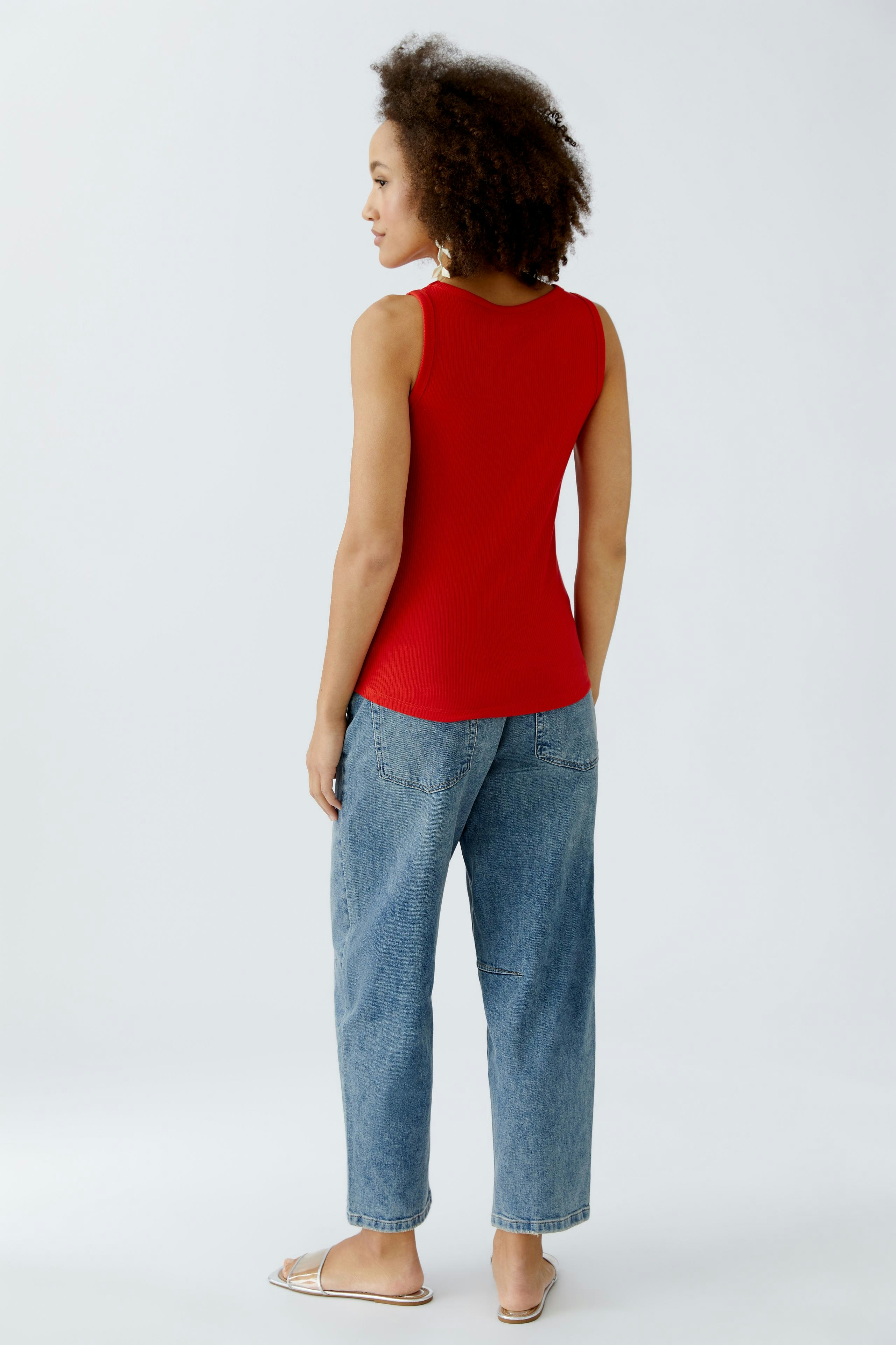 Casual women's top: Young woman in a red sleeveless top and relaxed jeans, standing confidently.