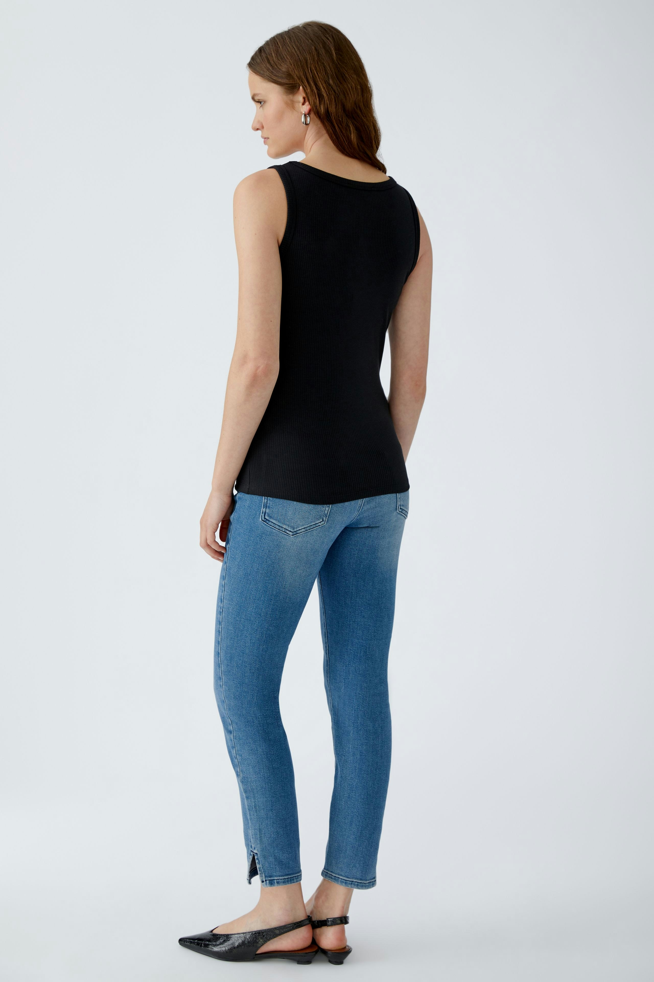 Casual women's top: A woman in a fitted black tank top and blue jeans stands confidently.