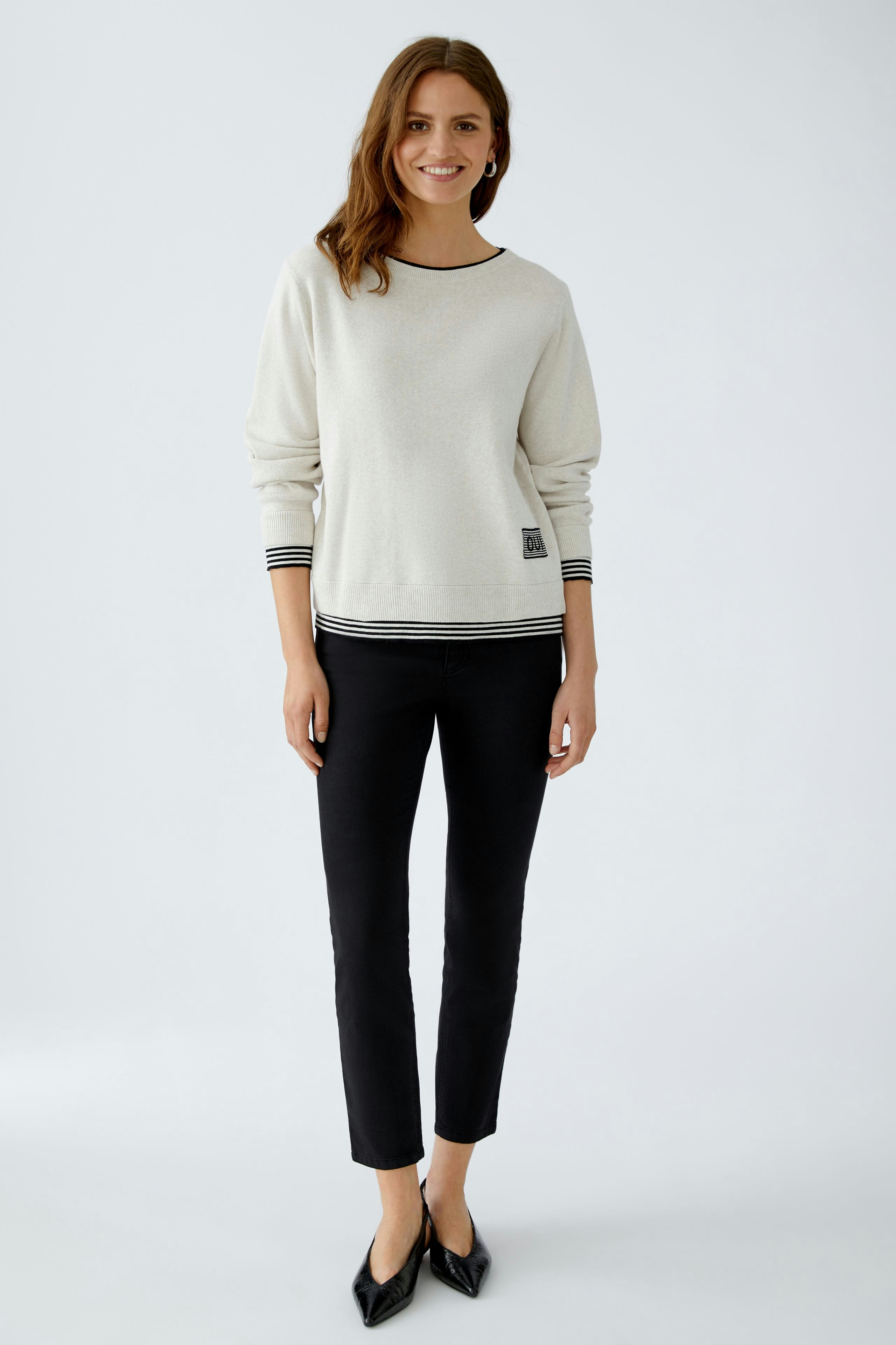 Modern women's pullover: A woman in a light pullover with striped details and black pants stands confidently.