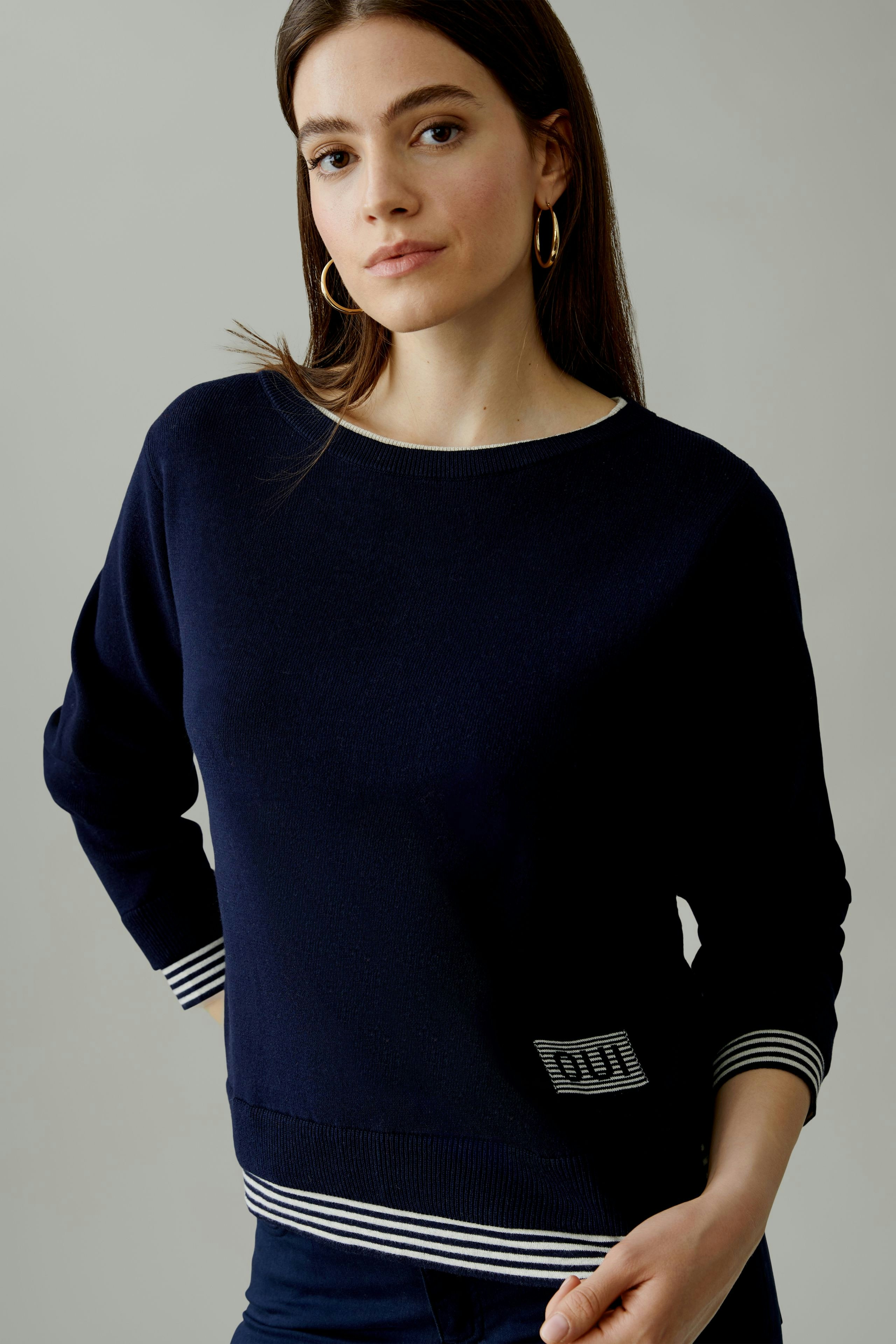 Casual women's pullover: Young woman in a navy pullover with striped cuffs, posing confidently.