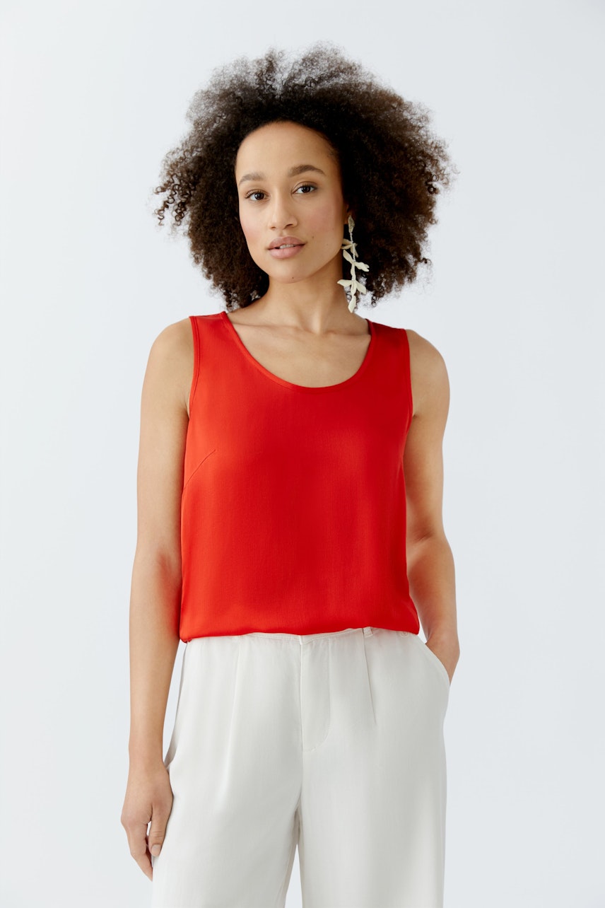 Casual women's top: A woman in a bright red sleeveless top paired with light trousers.