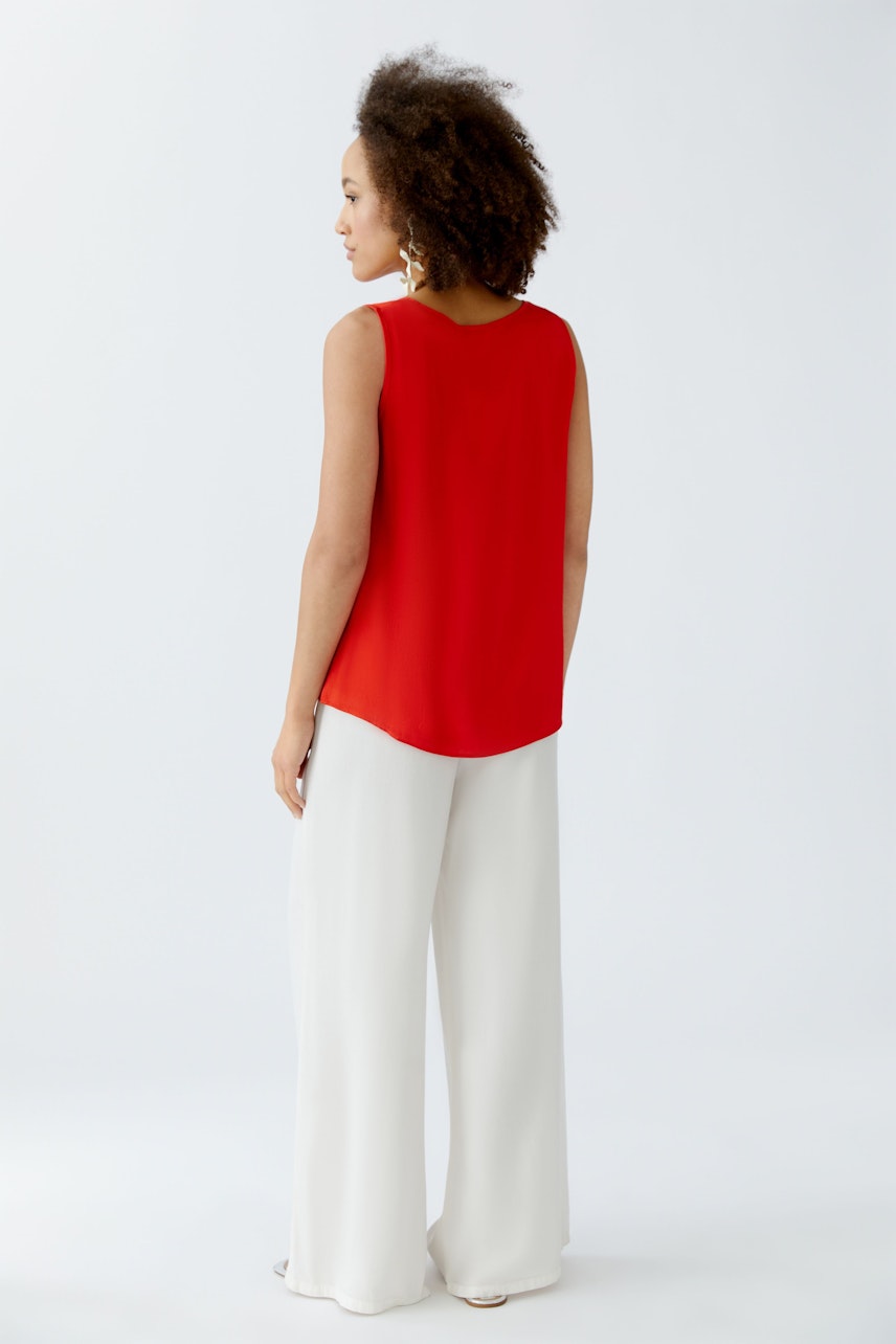 Casual women's top: A woman in a red sleeveless top paired with wide white pants, showcasing a relaxed style.