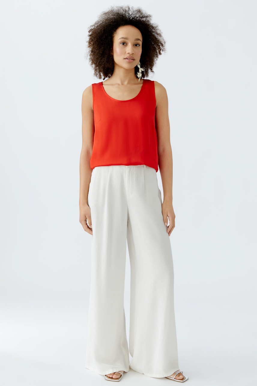 Casual women's top: A woman in a bright red sleeveless top paired with white wide-leg pants.