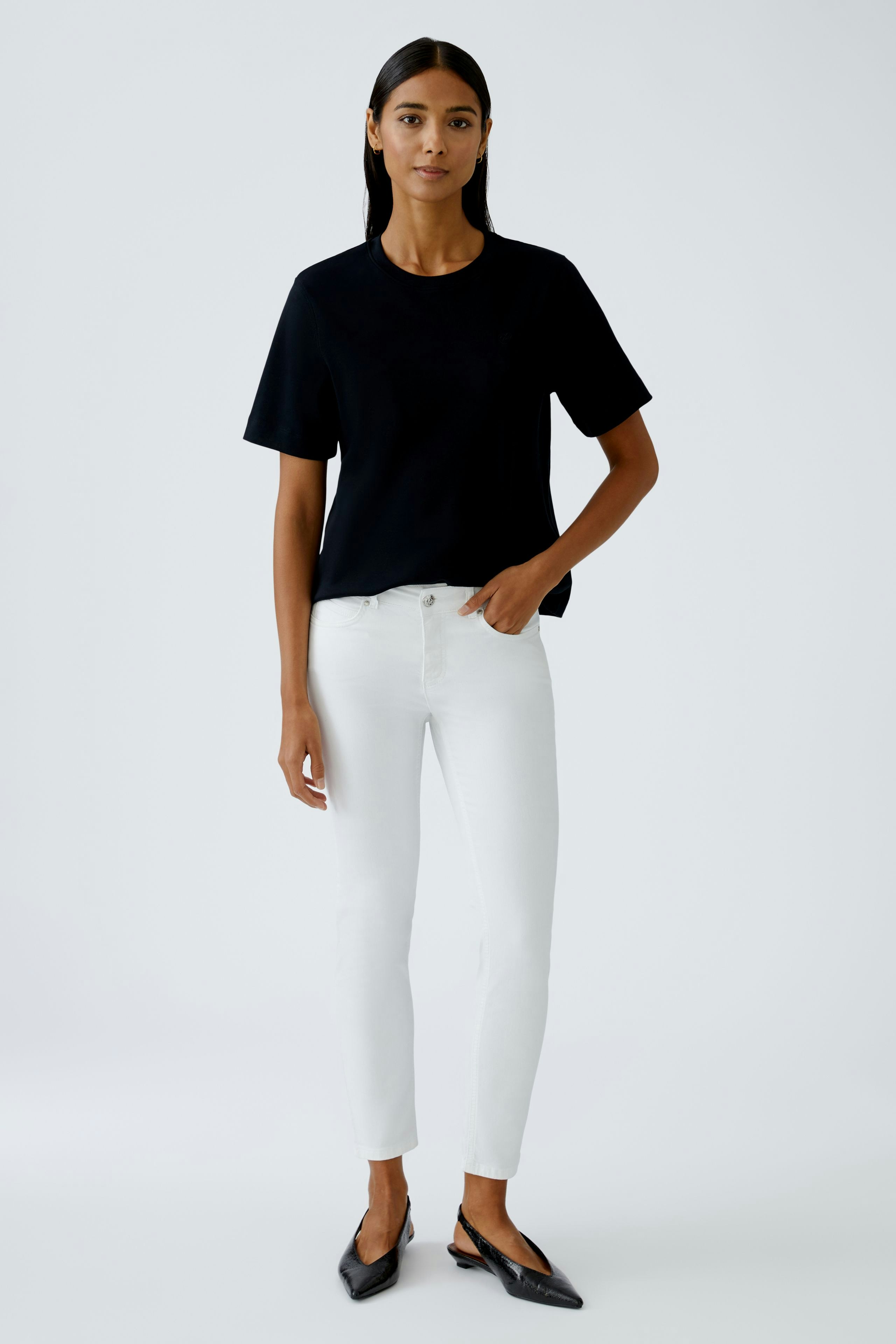 Moderne Jeggings: Junge Frau in weißen Jeggings und schwarzem Top steht lässig und selbstbewusst.