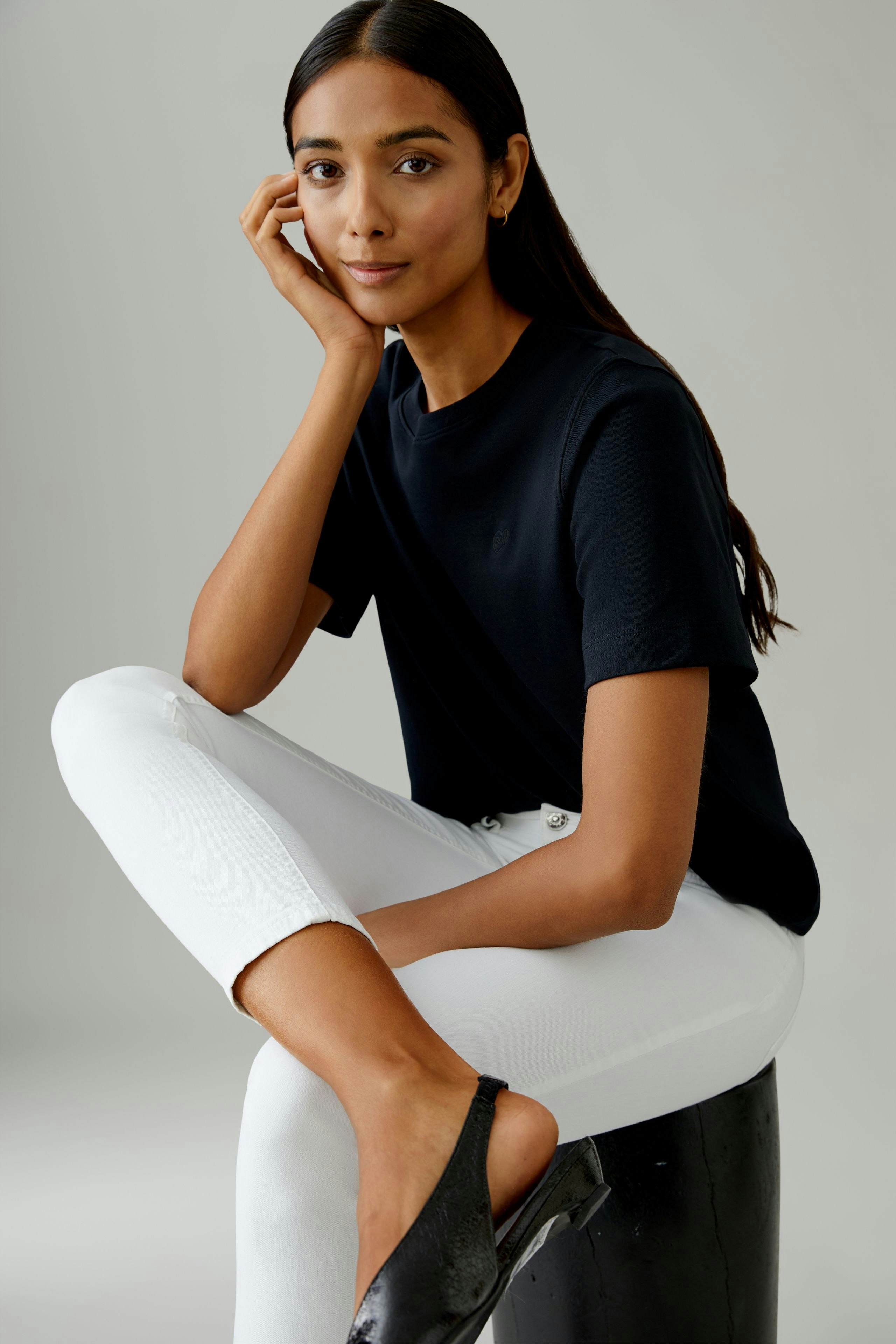 Bequeme Jeggings: Frau sitzt entspannt in weißen Jeggings und schwarzem T-Shirt, lässiger Look.