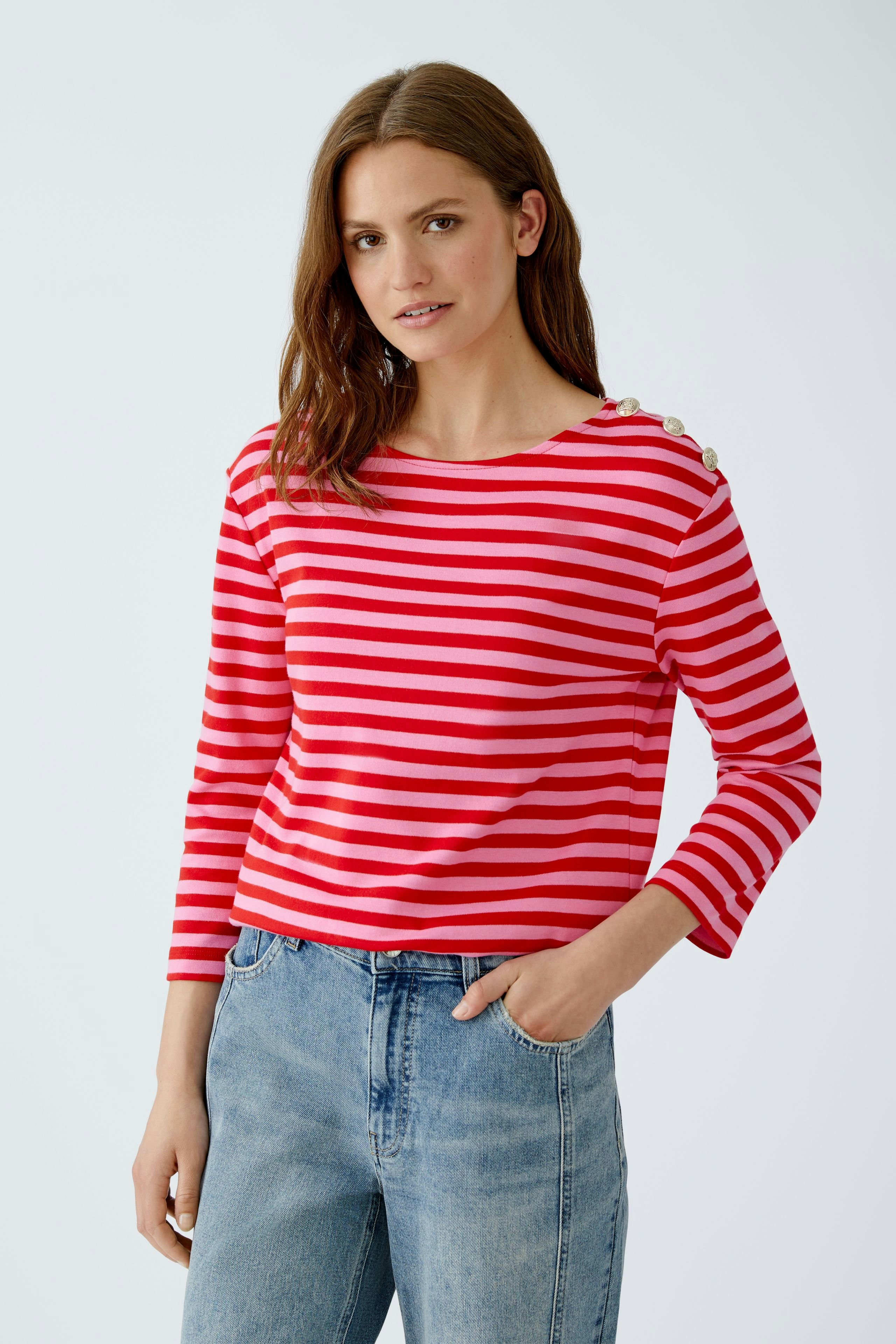 Damen Langarmshirt: Frau in gestreiftem Shirt mit Knöpfen an der Schulter und lässigen Jeans.