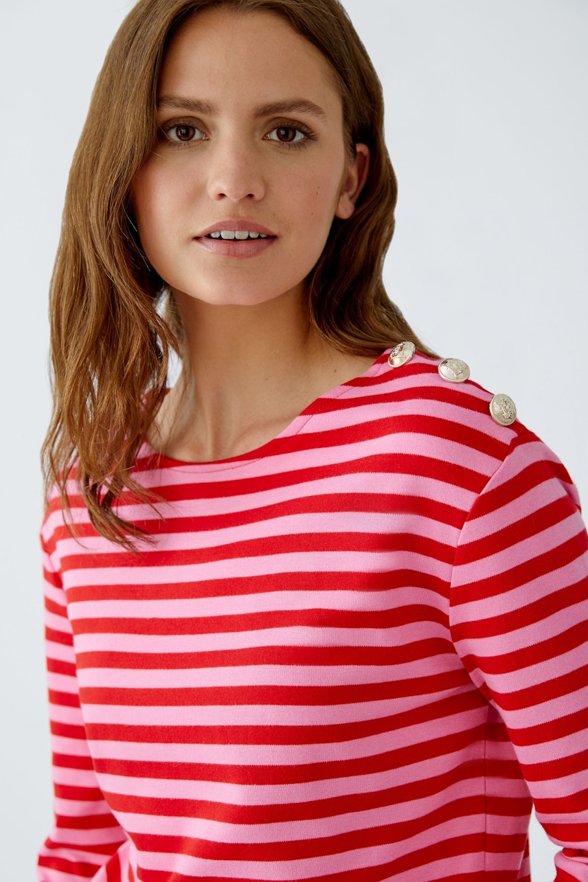 Casual long-sleeve shirt: Woman in a red and pink striped pullover with button details.