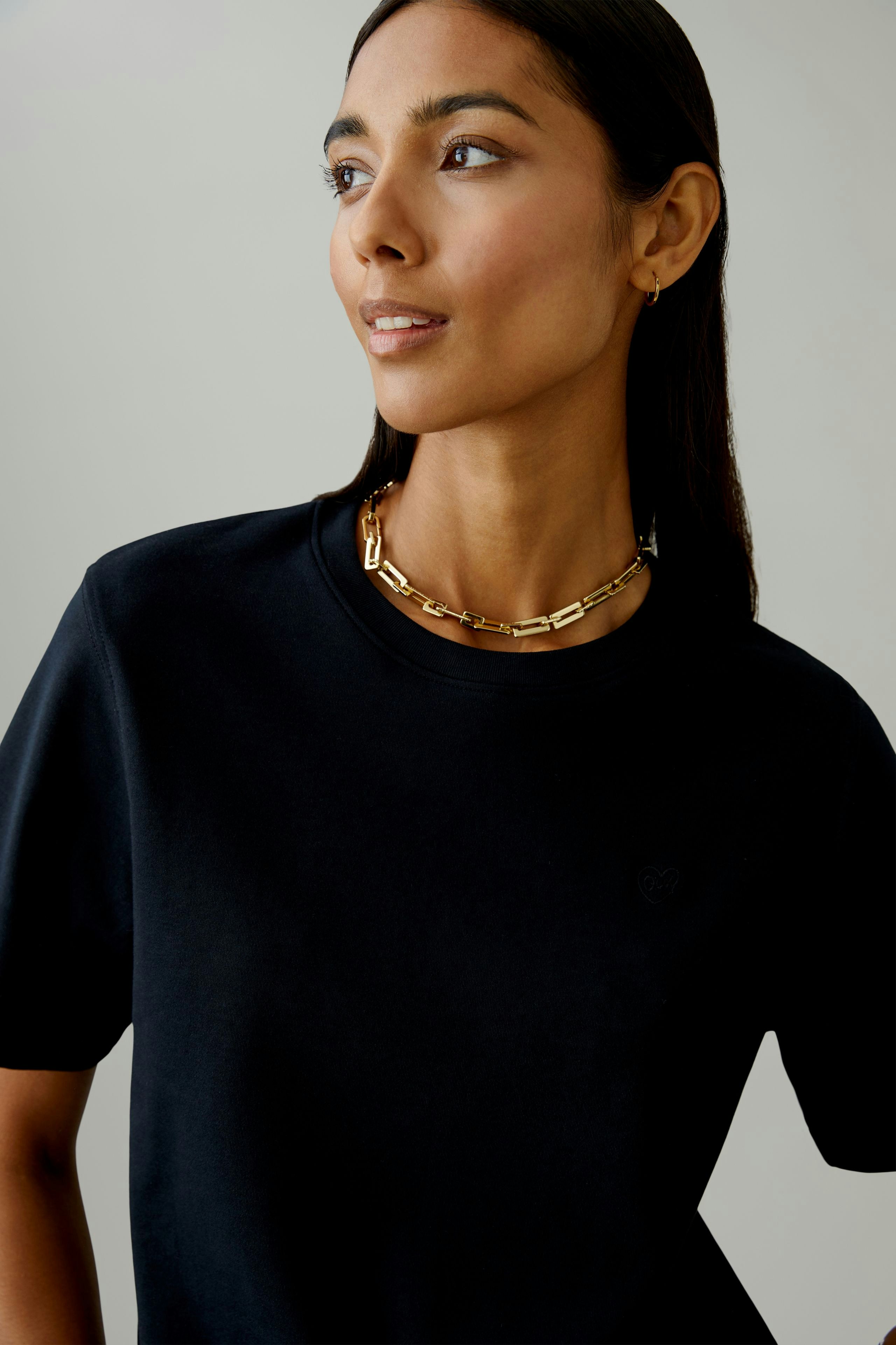 Schwarzes Damen-T-Shirt: Frau mit kurzem Arm und goldener Kette lächelt selbstbewusst.