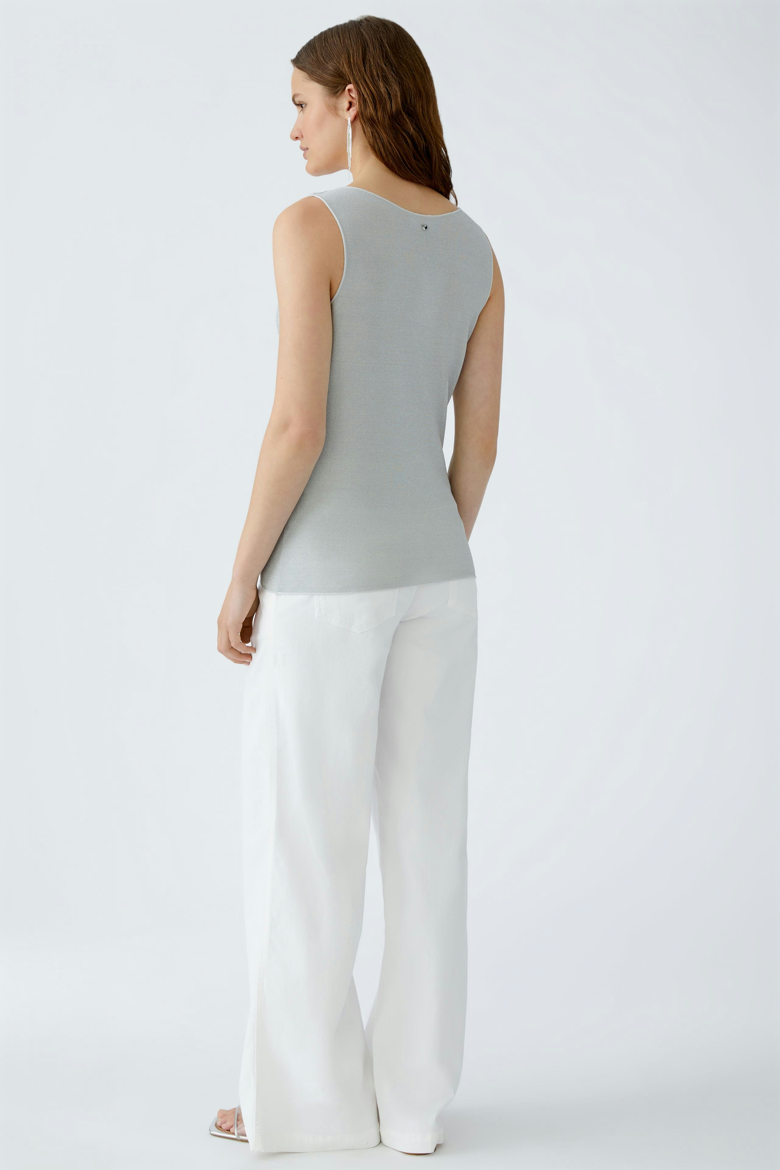 Beige Damen-Tank Top: Frau trägt ein ärmelloses, graues Top mit lässiger Passform und weißen Hosen.