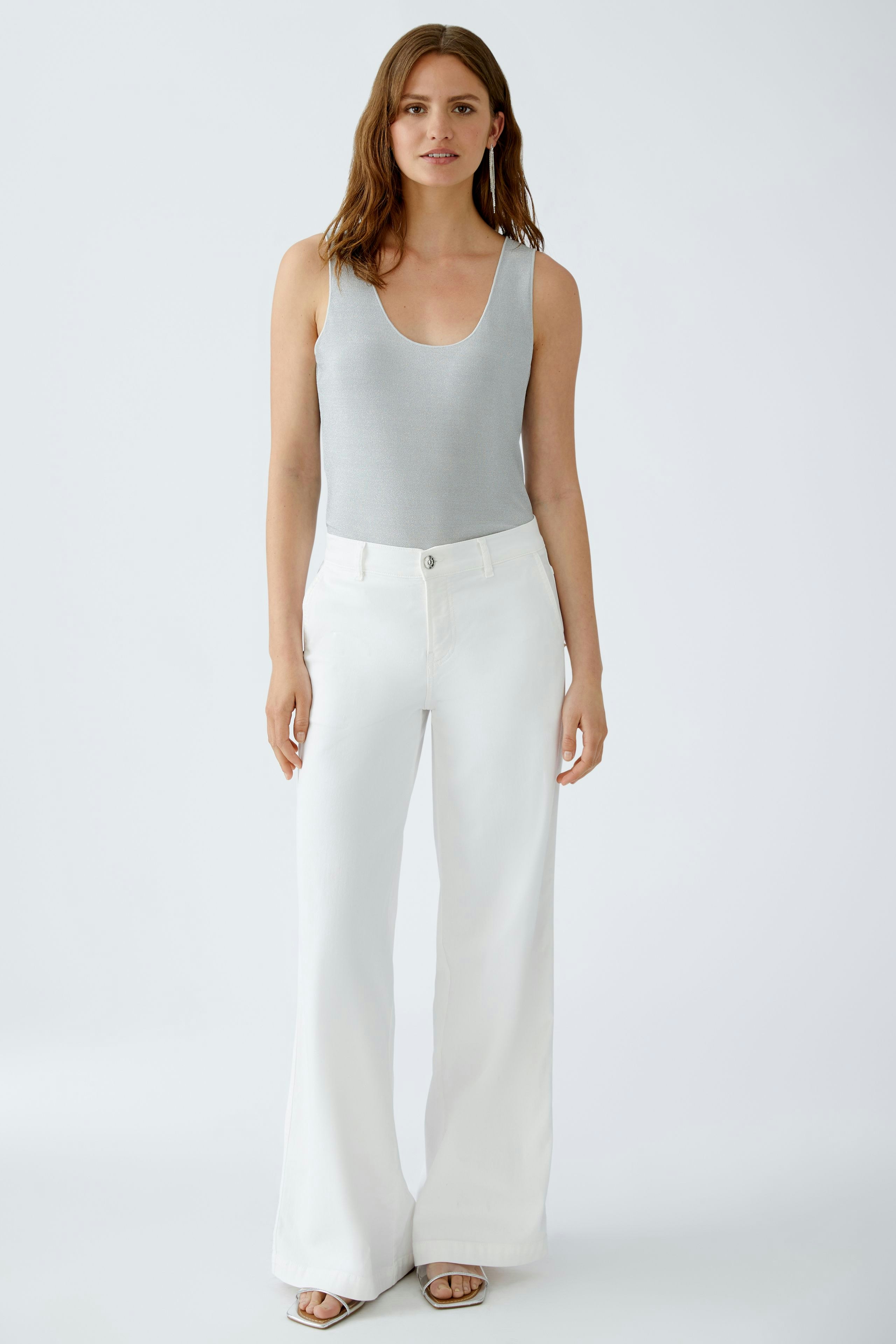 Bequemer Damen-Tank Top: Frau in grauem Top und weißen, weiten Hosen steht entspannt.