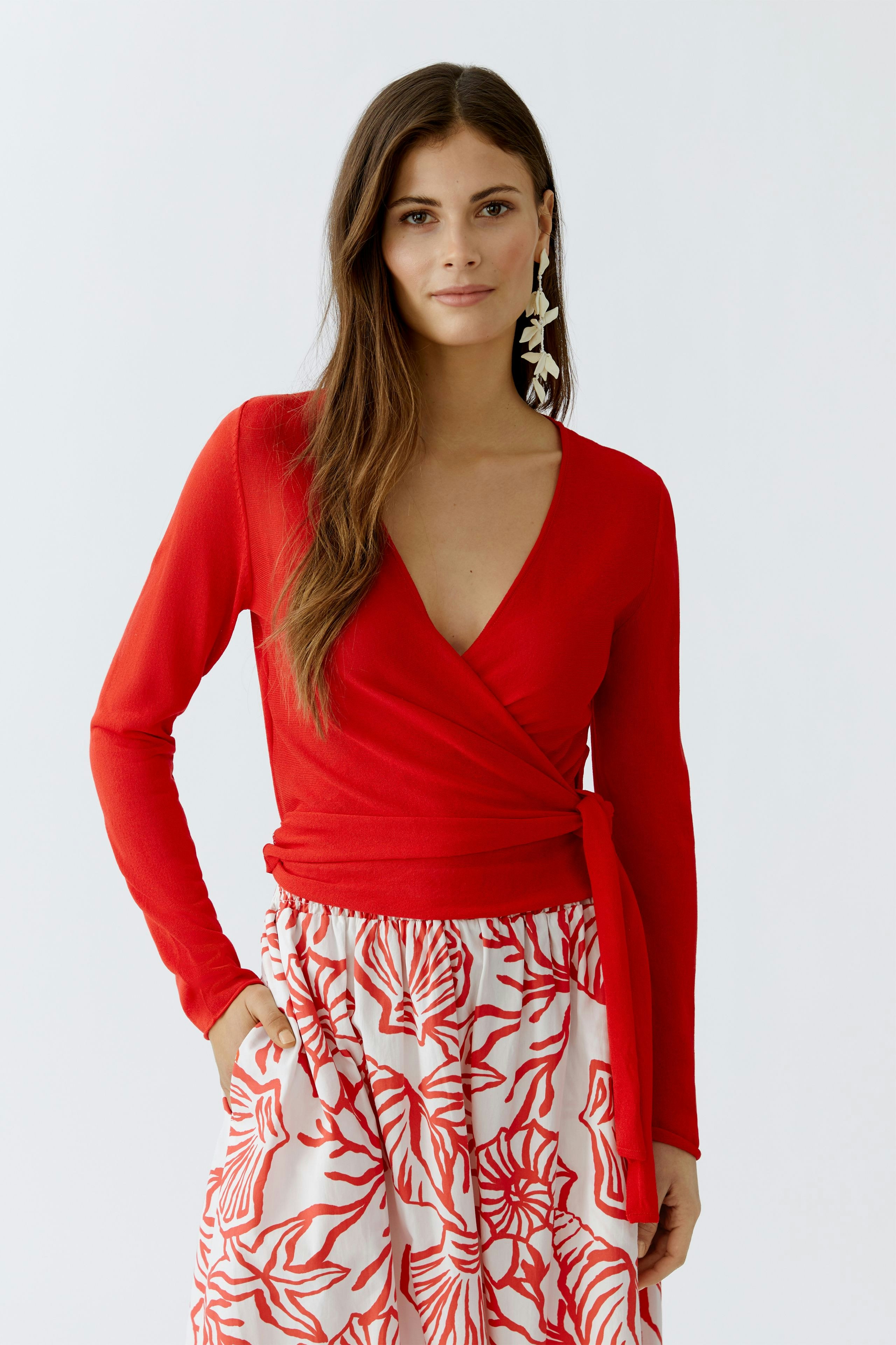 Rote Damen-Strickjacke: Frau mit langen Haaren trägt eine figurbetonte Jacke über einem gemusterten Rock.