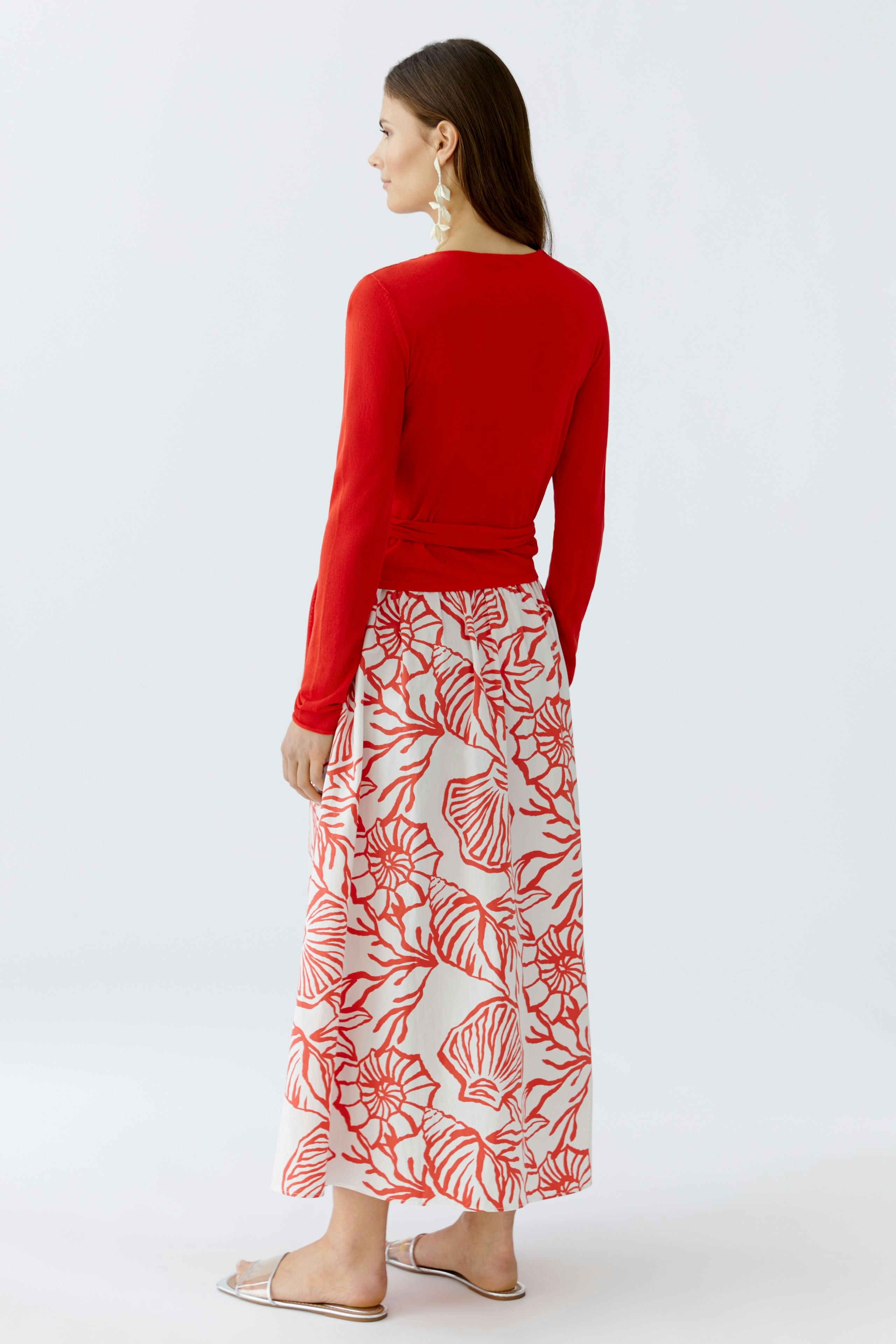 Damen-Strickjacke: Frau in roter Strickjacke mit floralem Rock, von hinten betrachtet.