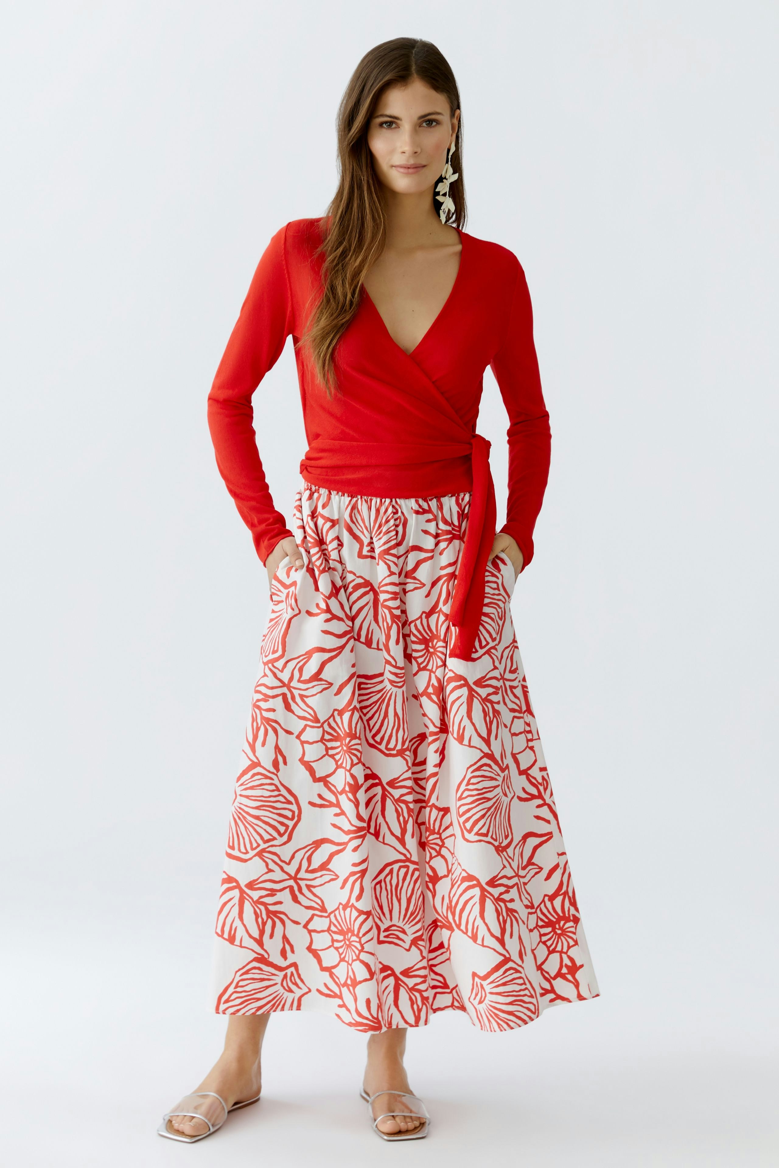 Rote Strickjacke: Frau in roter Wickeljacke kombiniert mit einem floralen Rock.