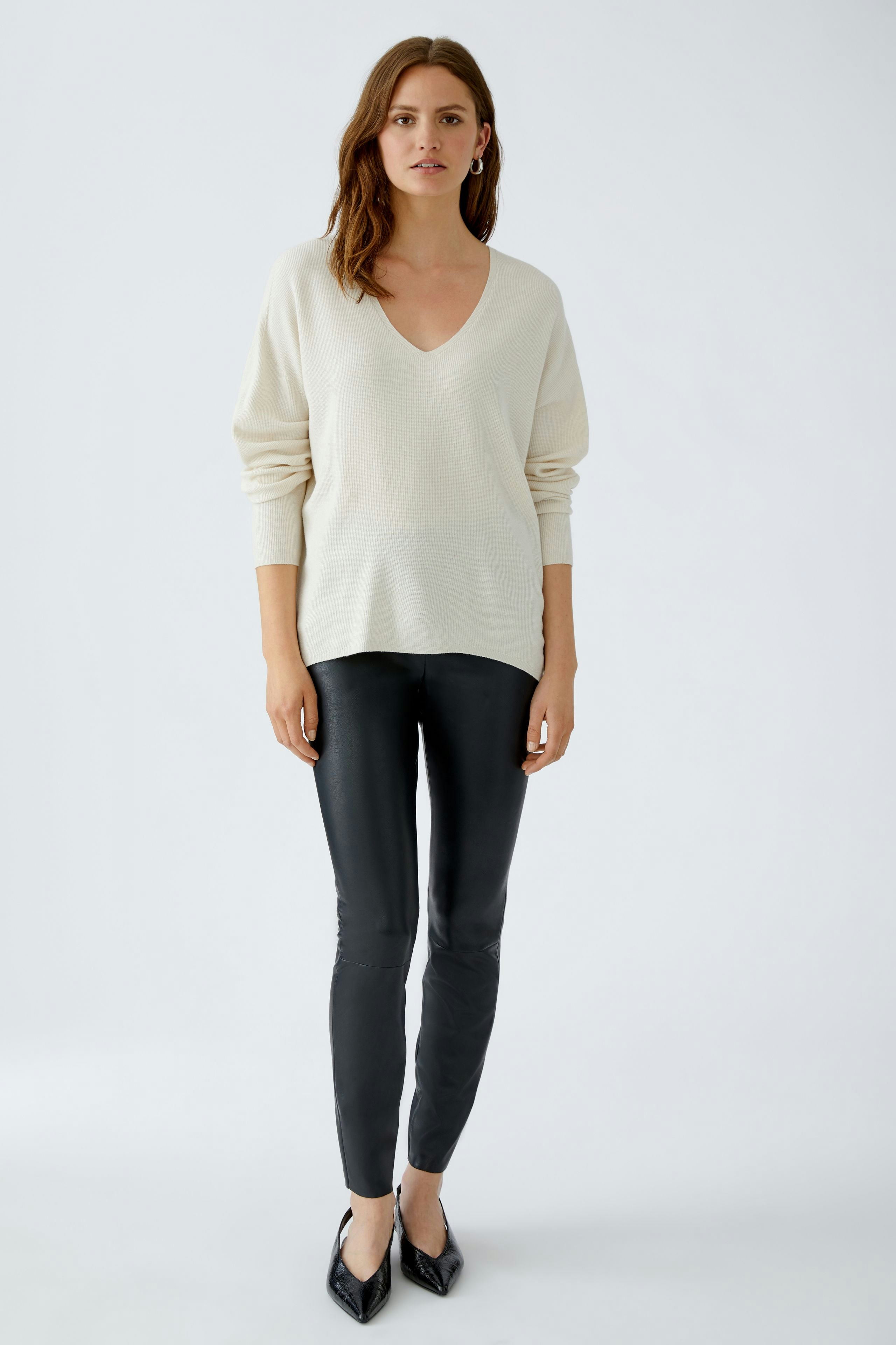 Damen-Pullover: Junge Frau in beigem V-Pullover kombiniert mit schwarzen Leggings und eleganten Schuhen.