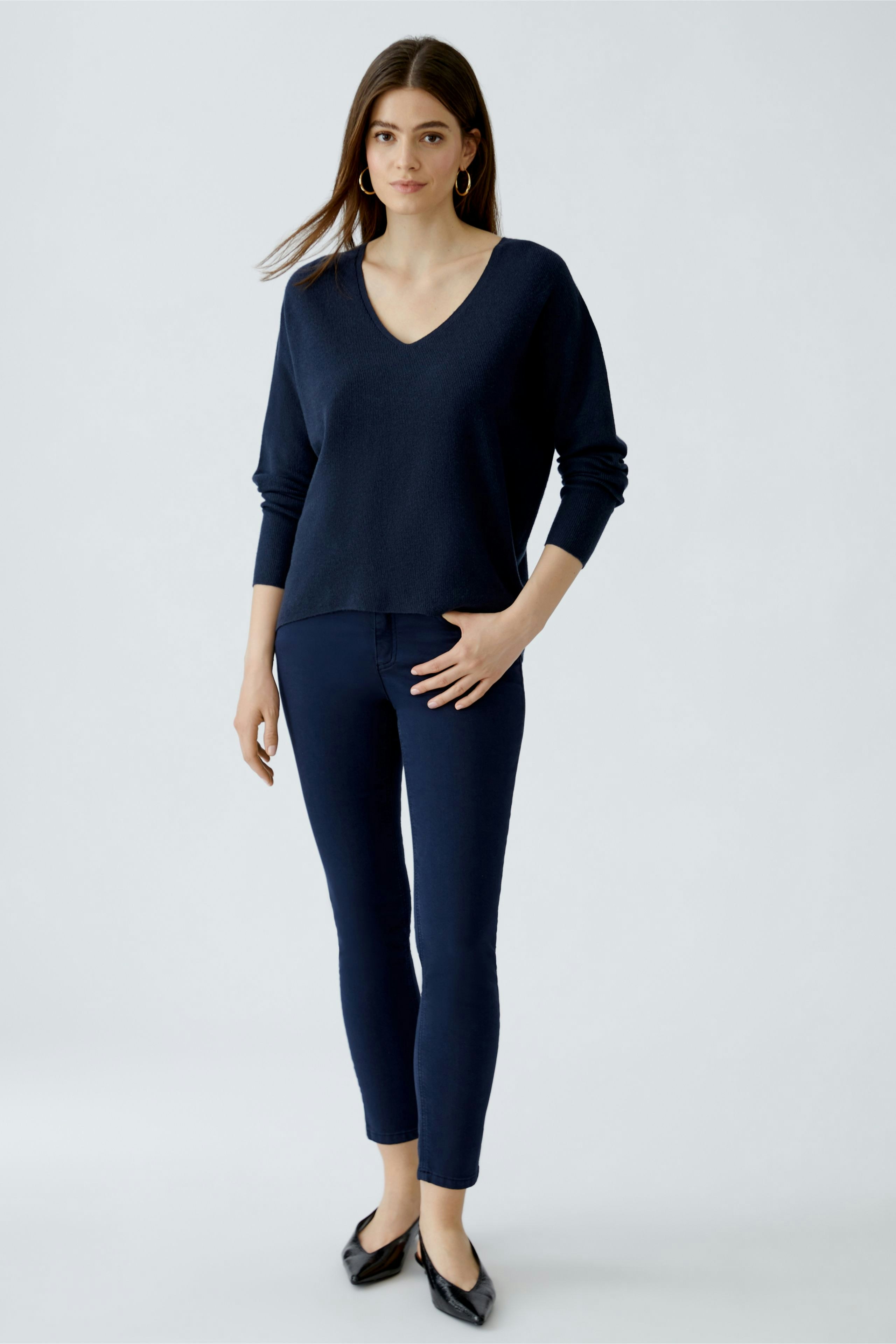 Casual women's pullover: Young woman in a navy V-neck pullover paired with fitted jeans.