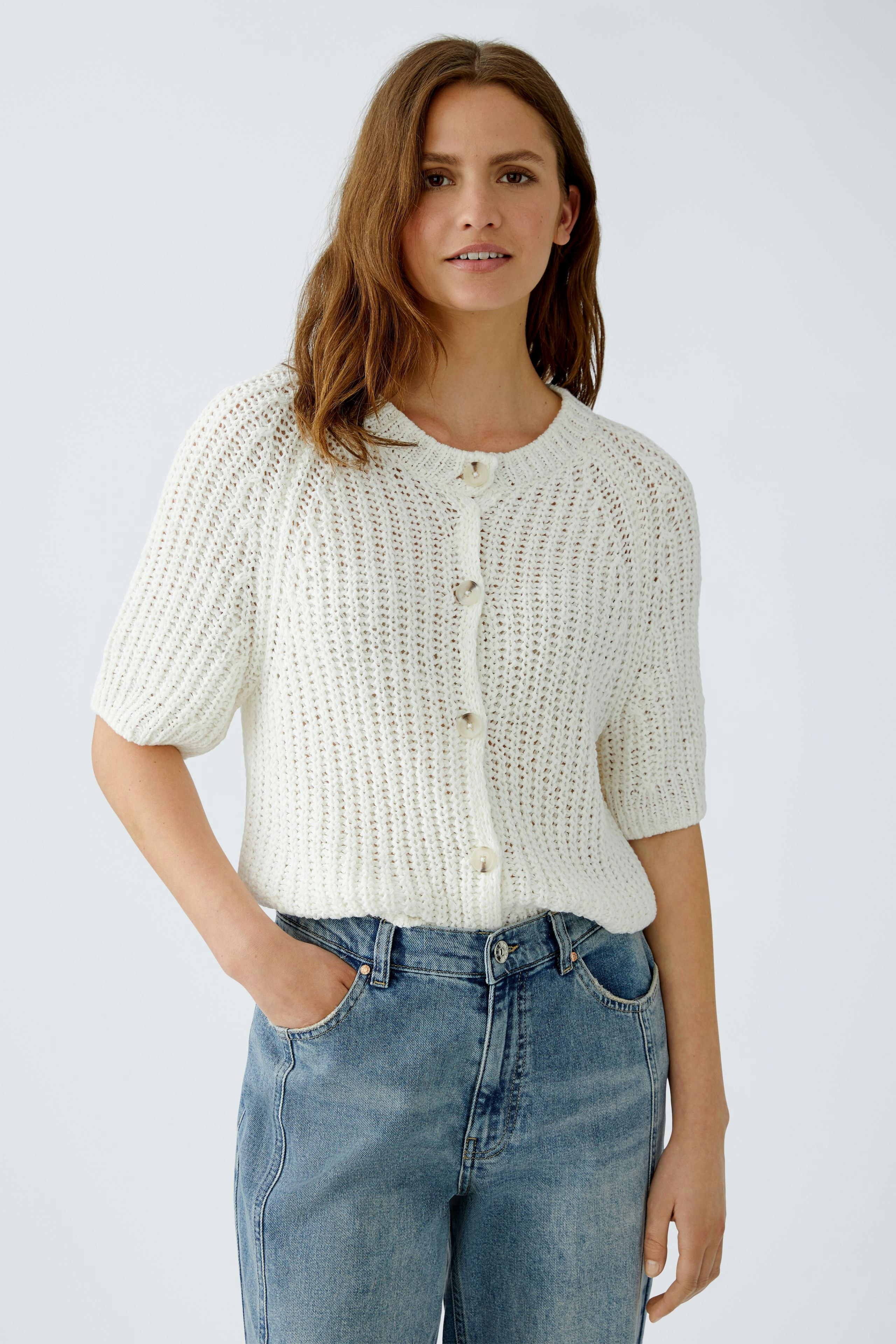 Casual women's cardigan: A woman in a white knitted cardigan with buttons and relaxed jeans.