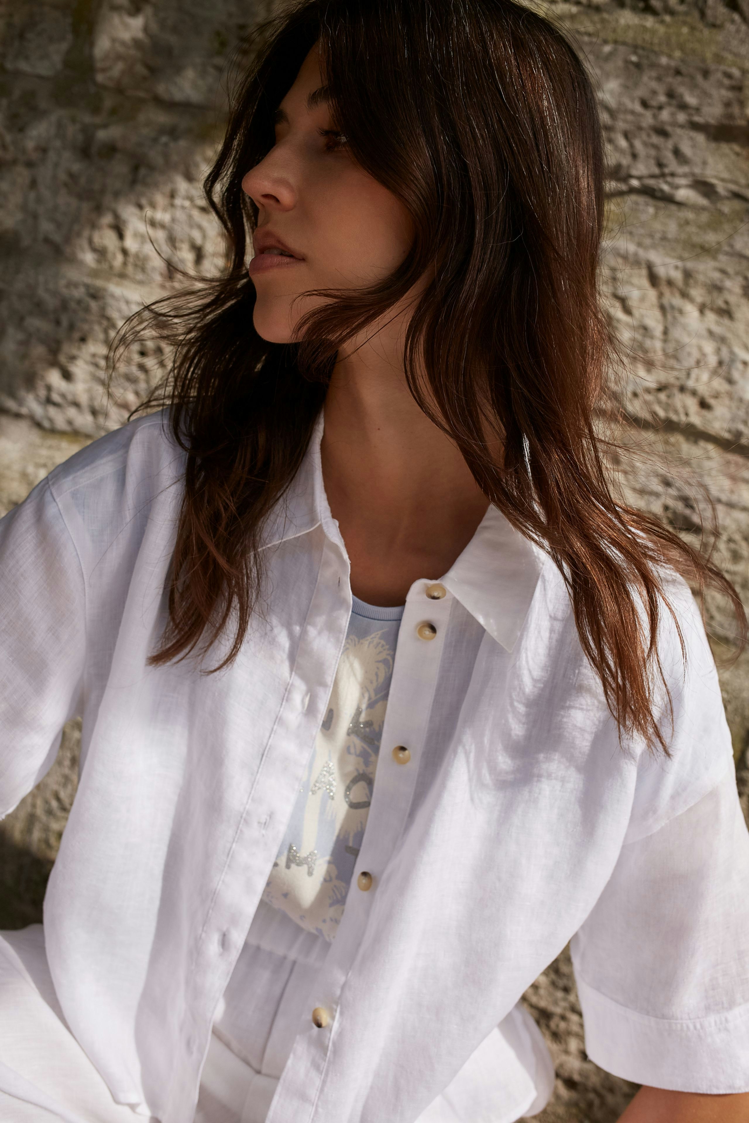 Casual women's blouse: Woman in a white button-up blouse with a relaxed fit, styled effortlessly.