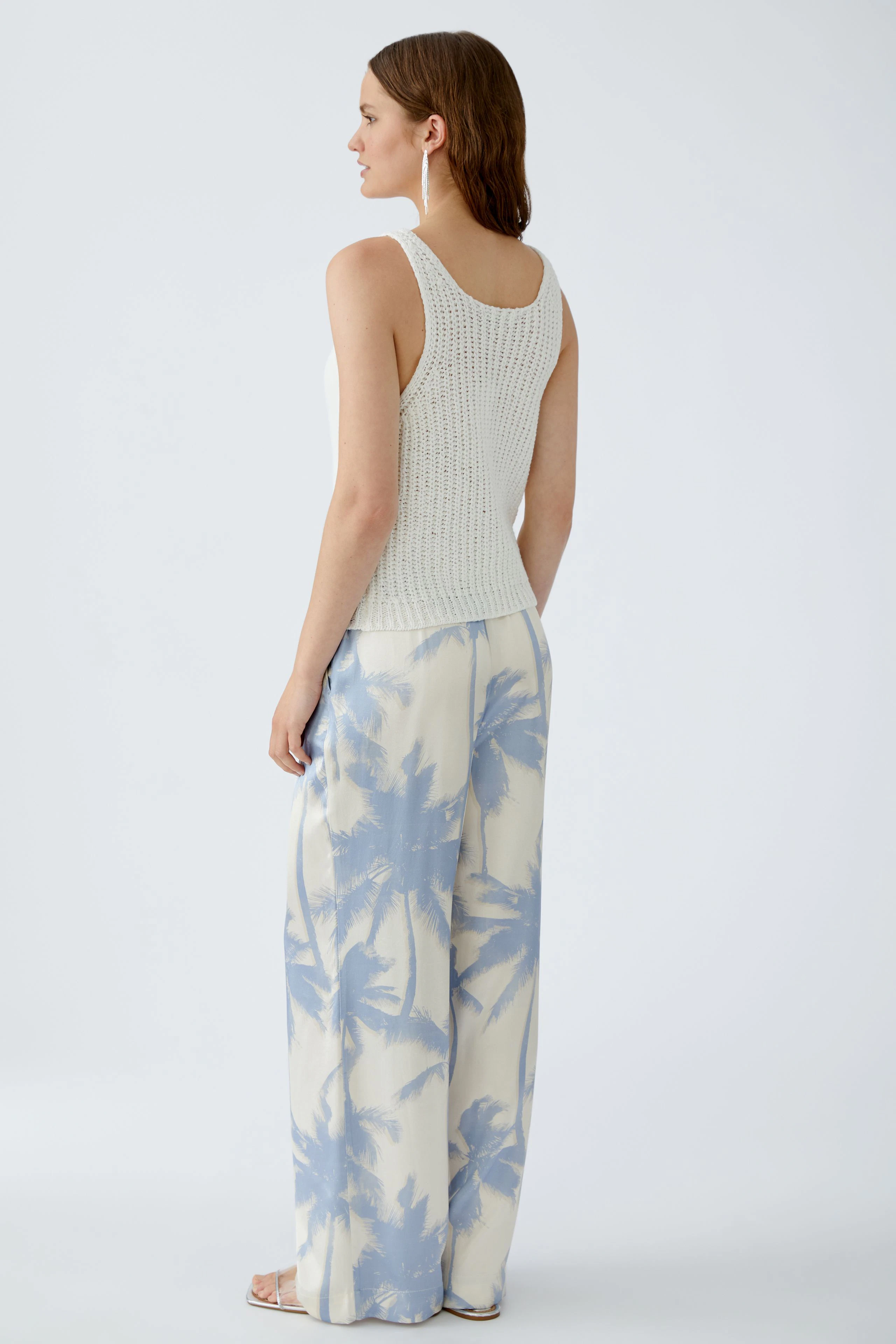 Damen-Top: Junge Frau in einem hellen, gestrickten Top mit lässigen, weiten Hosen im Palmen-Design.