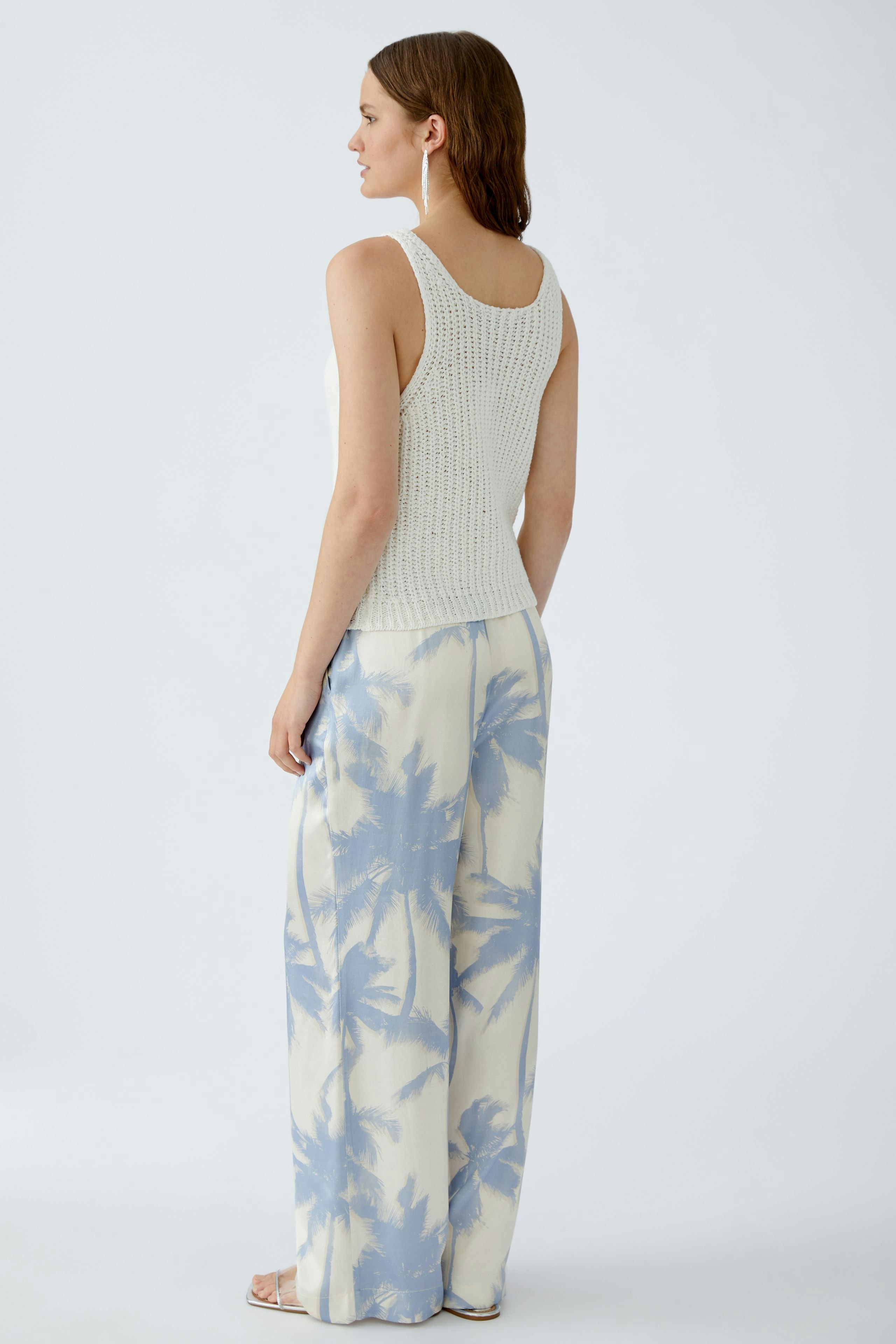 Damen-Top: Junge Frau in einem hellen, gestrickten Top mit lässigen, weiten Hosen im Palmen-Design.