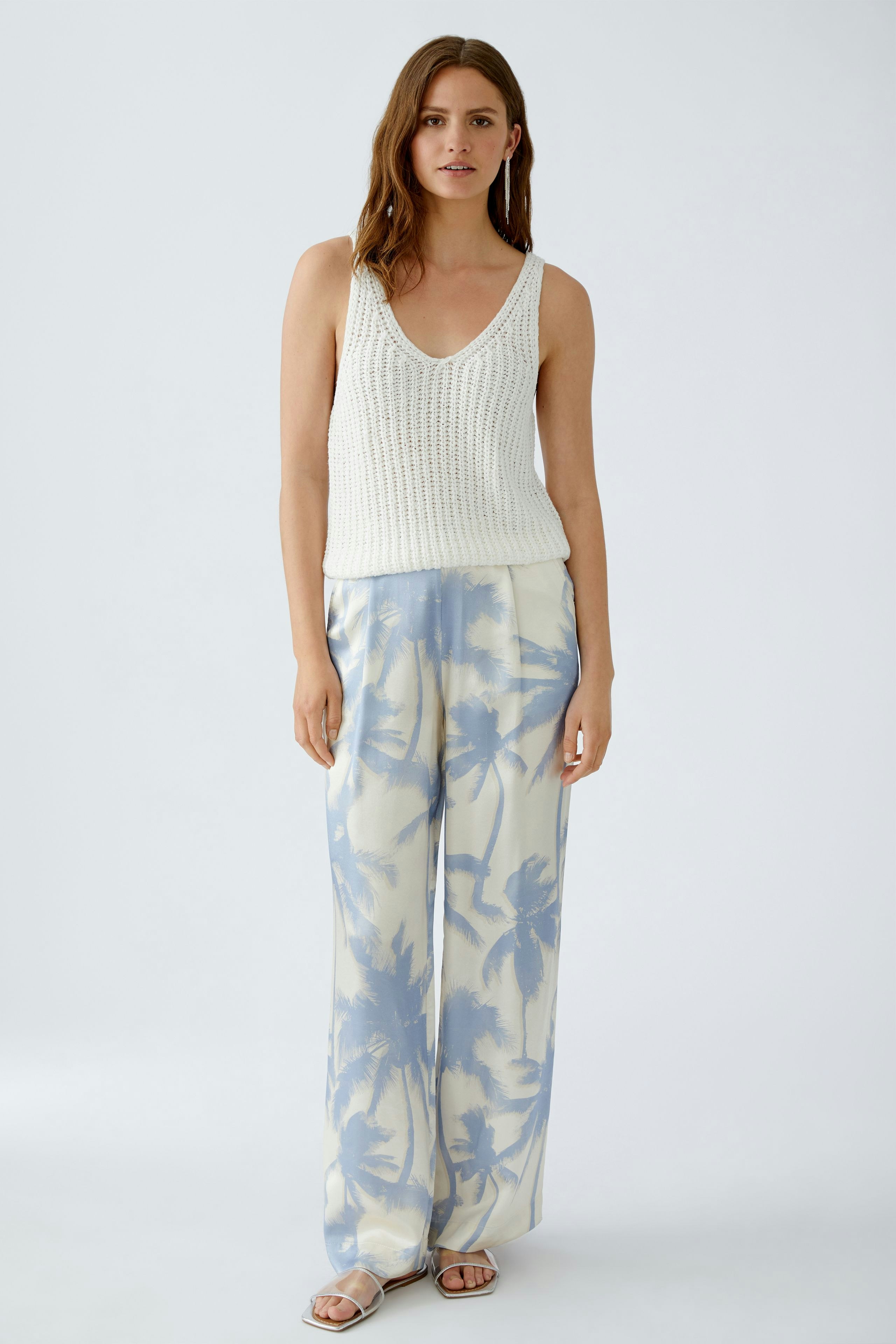 Lässiges Damen-Top: Junge Frau in einem weißen, gestrickten Top mit V-Ausschnitt und lockeren Hosen.