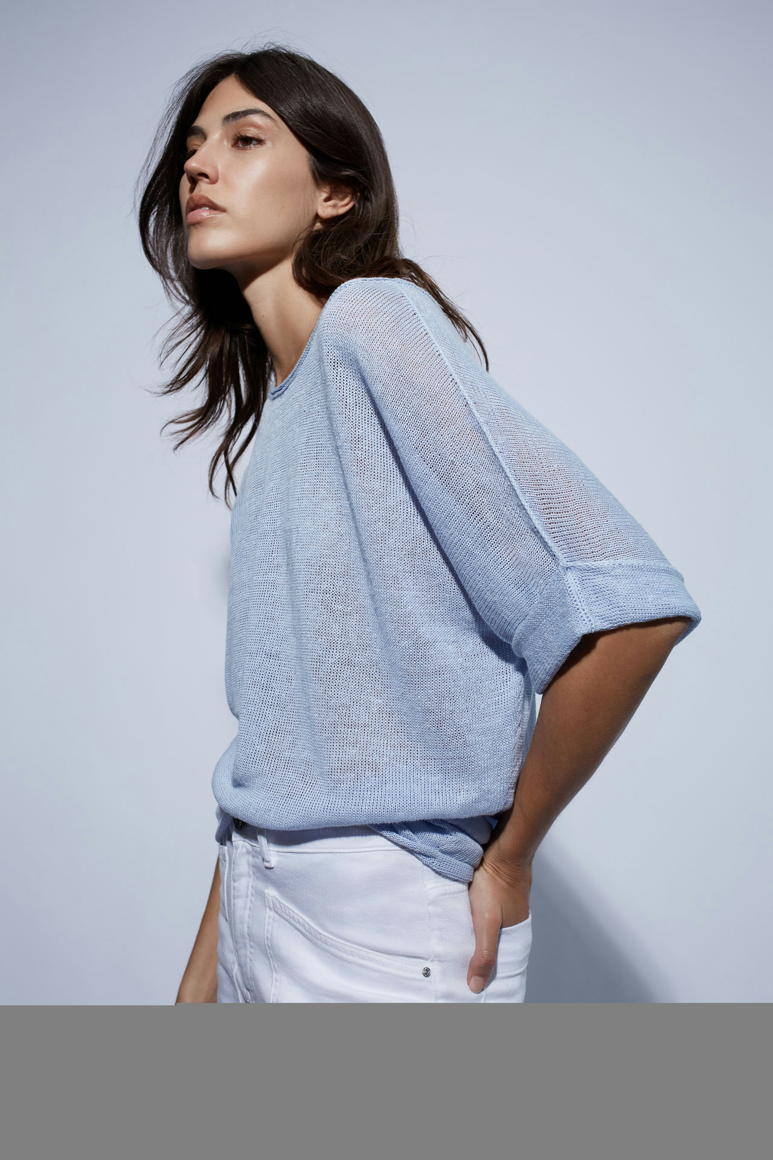 Bequeme Damen-Jeans Tapered: Frau in hellblauen Jeans und lässigem Pullover mit überschnittenen Ärmeln.