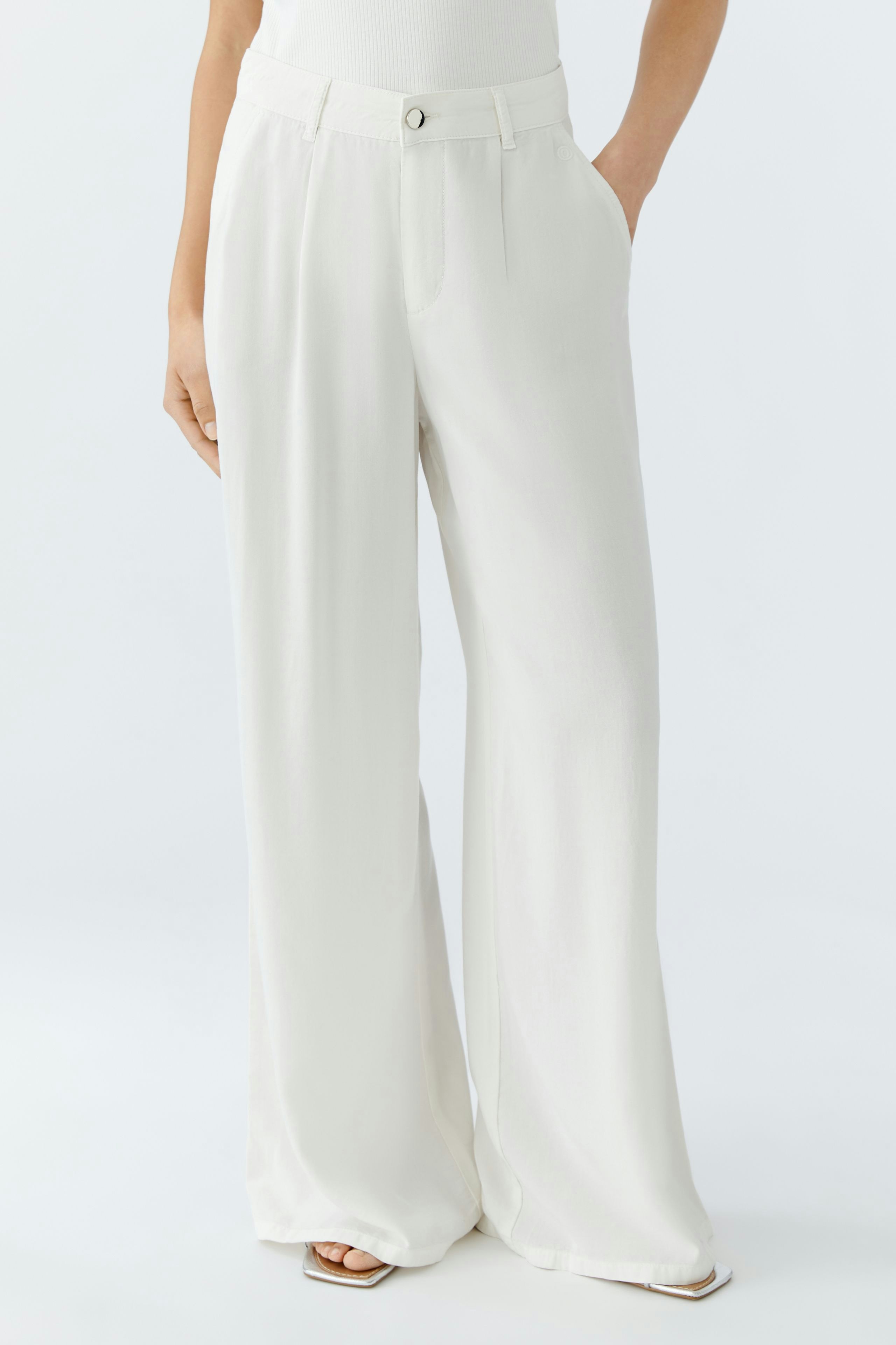 Bequeme Bundfaltenhose: Frau trägt eine weiße, weite Hose mit Taschen und einem Knopfverschluss.
