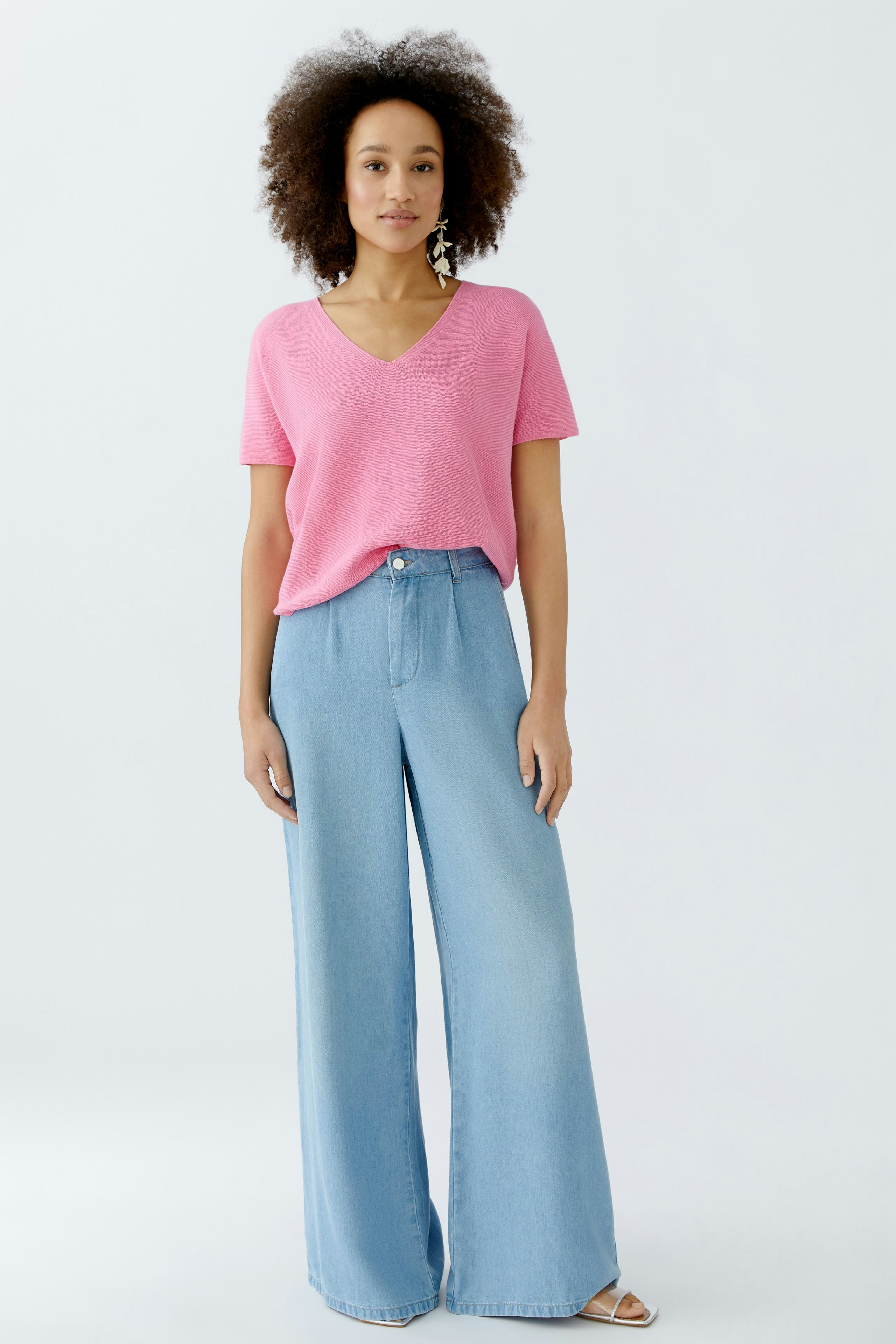 Casual women's pullover: A woman in a pink V-neck pullover paired with wide-leg jeans.