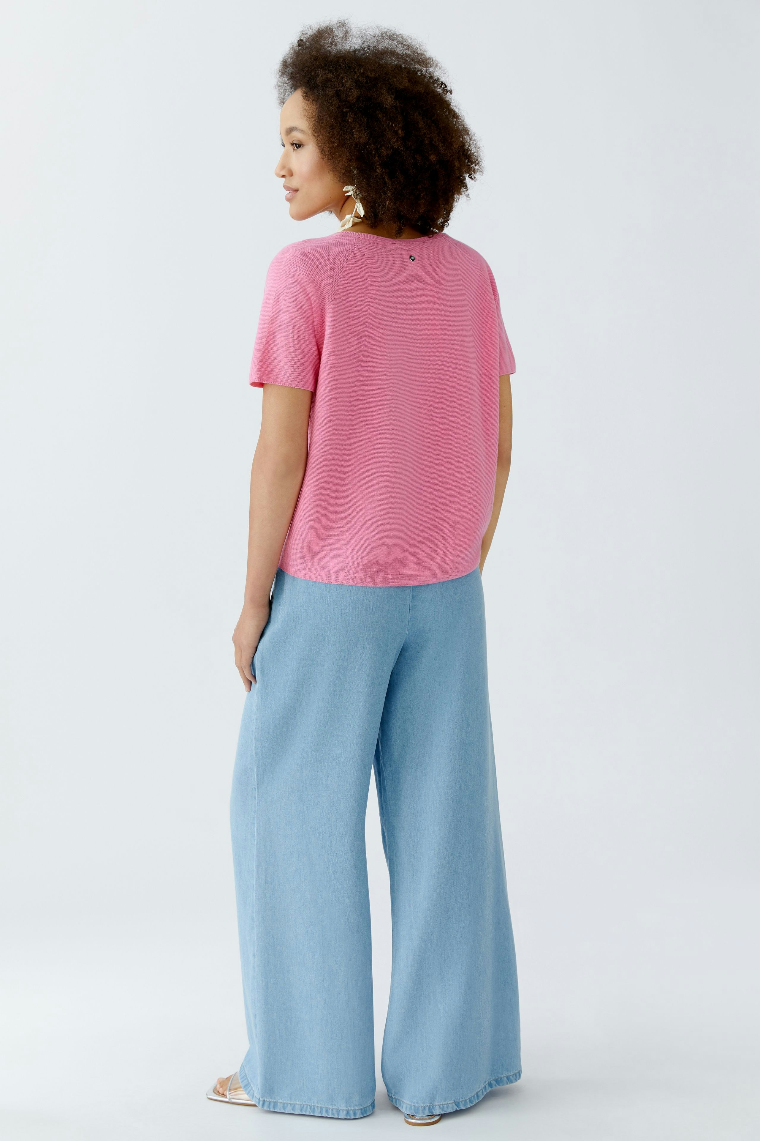 Casual women's pullover: Young woman in a pink short-sleeve pullover and wide denim pants.