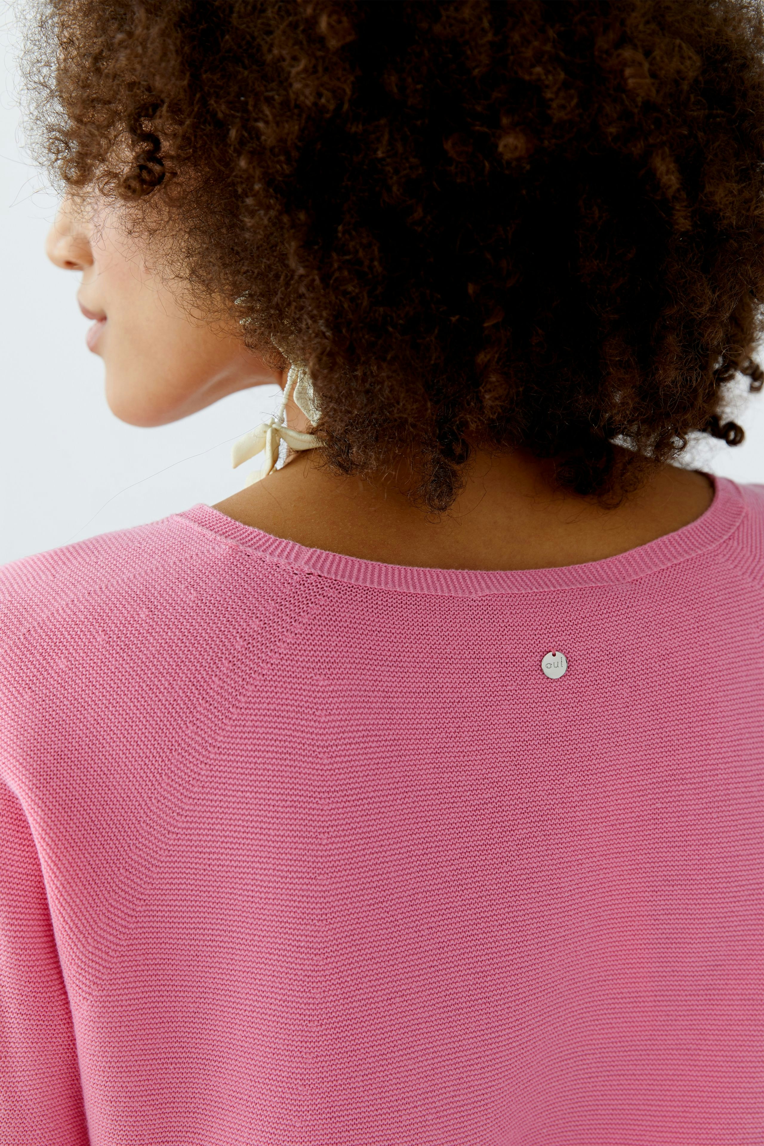 Casual women's pullover: A woman with curly hair wearing a pink pullover, showcasing a simple design.