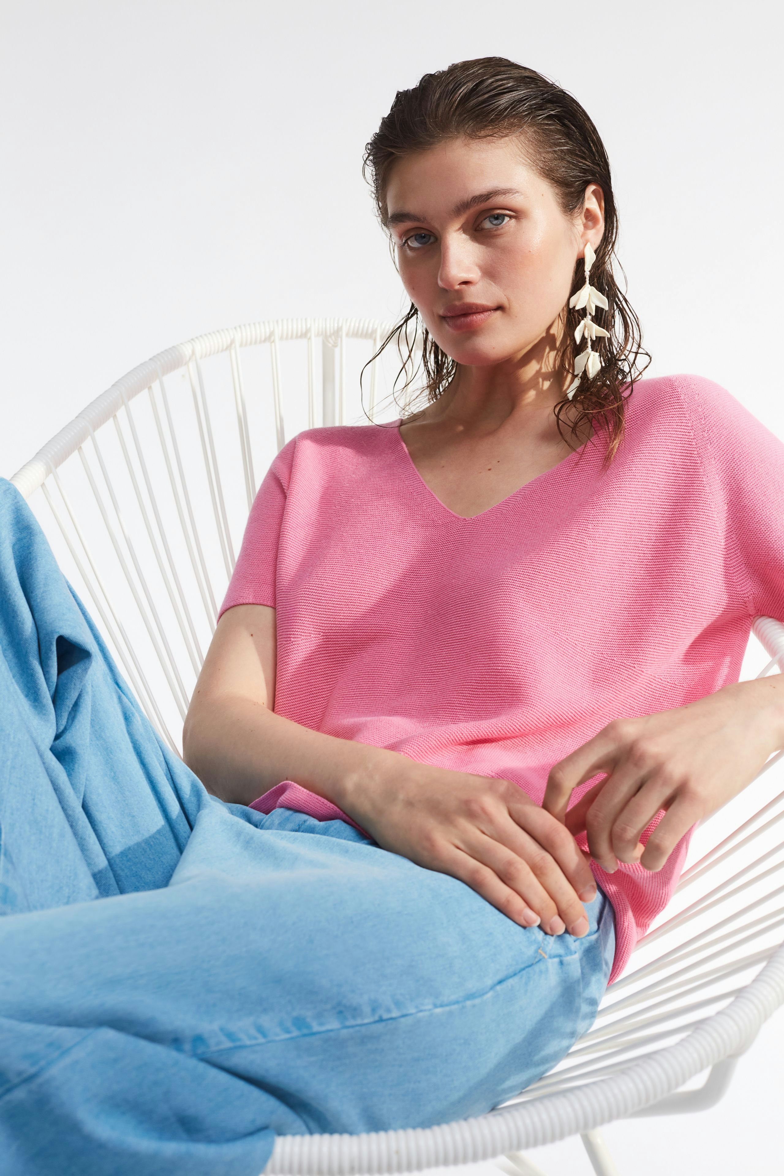 Casual women's pullover: Young woman in a pink V-neck pullover, relaxed in blue pants.
