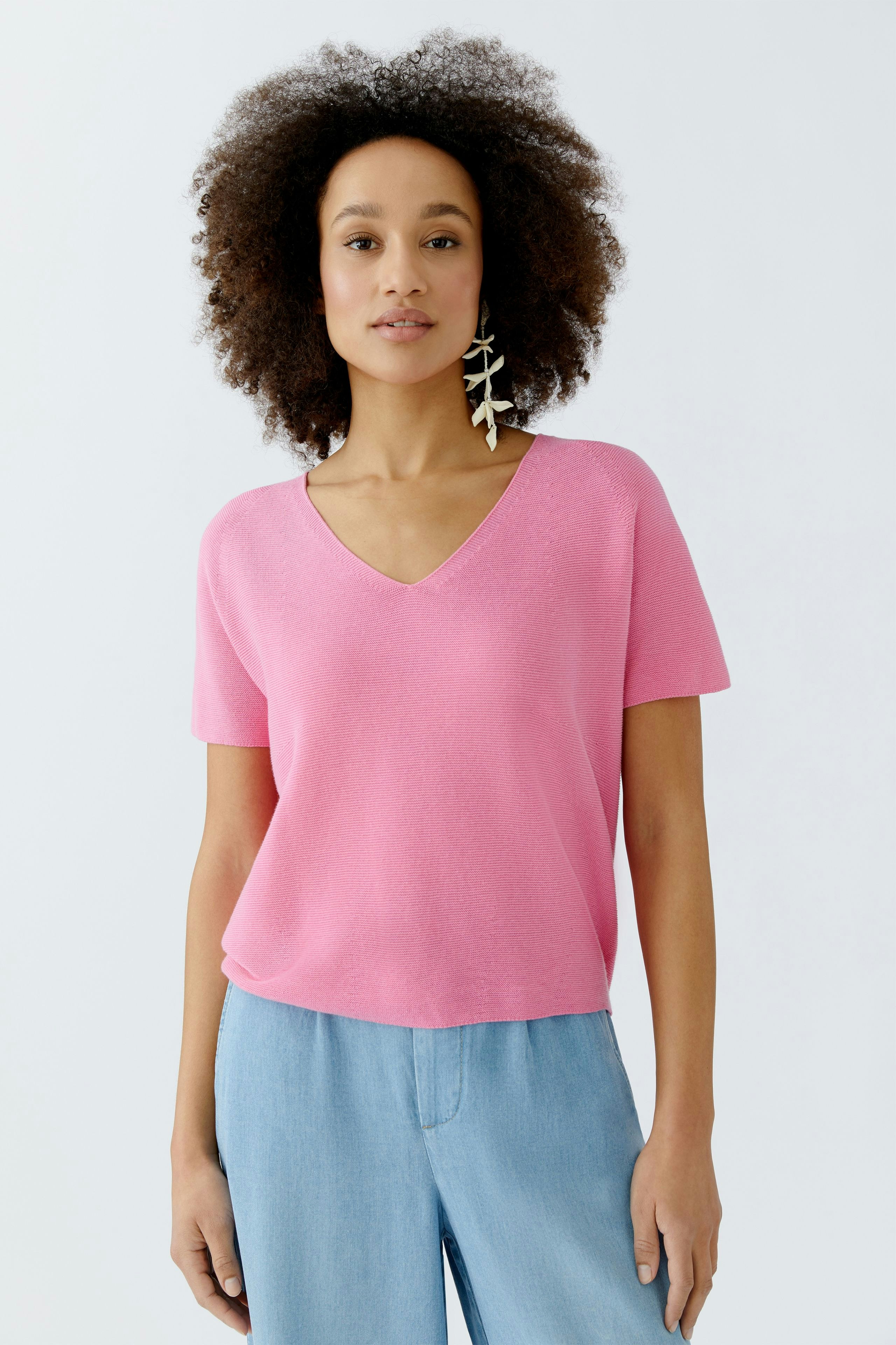 Casual women's pullover: A woman in a pink V-neck pullover paired with light blue pants.
