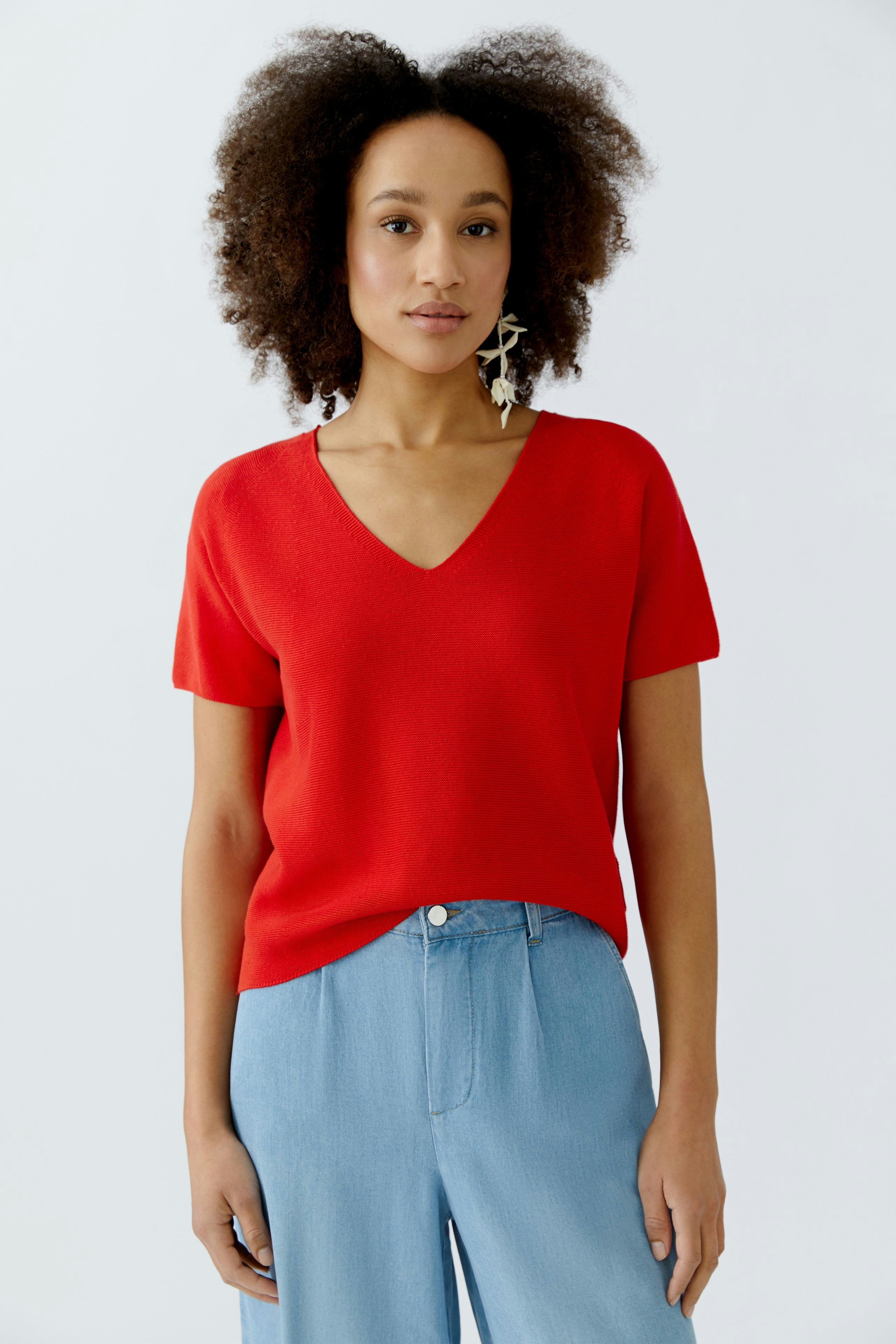 Roter Damen-Pullover mit V-Ausschnitt, lässig kombiniert mit hellblauen Hosen.