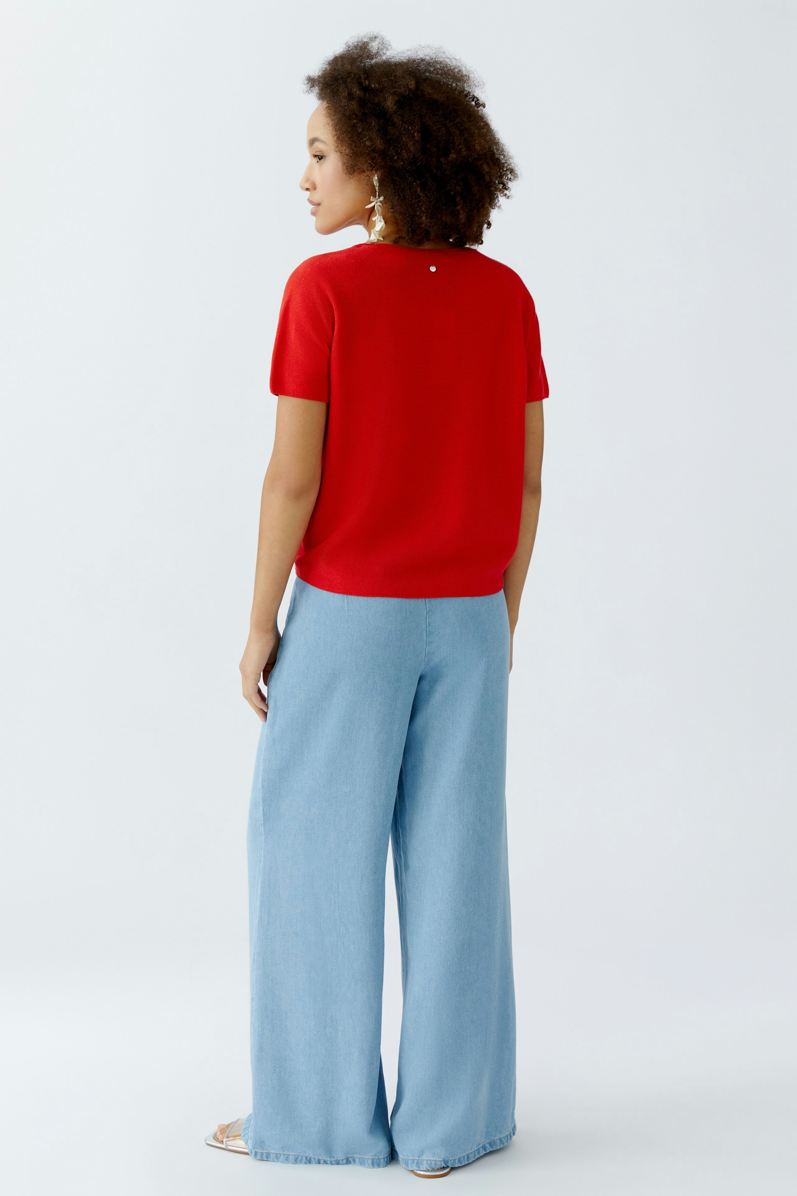 Damen-Pullover: Frau in rotem, lässigem Pullover mit kurzen Ärmeln und weitem Schnitt, von hinten sichtbar.