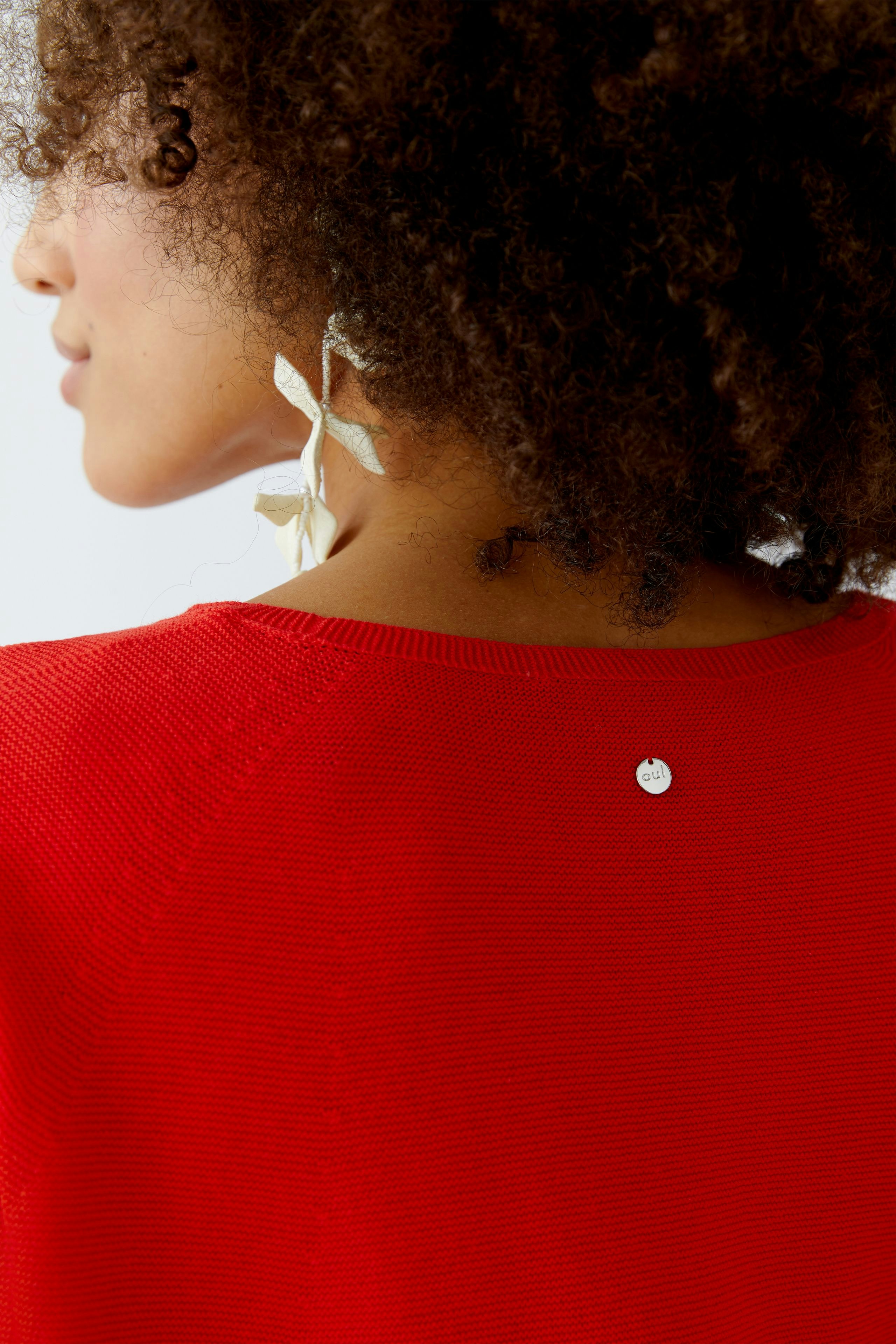 Damen-Pullover in leuchtendem Rot: Frau mit lockigem Haar trägt den Pullover mit dezentem Detail am Rücken.