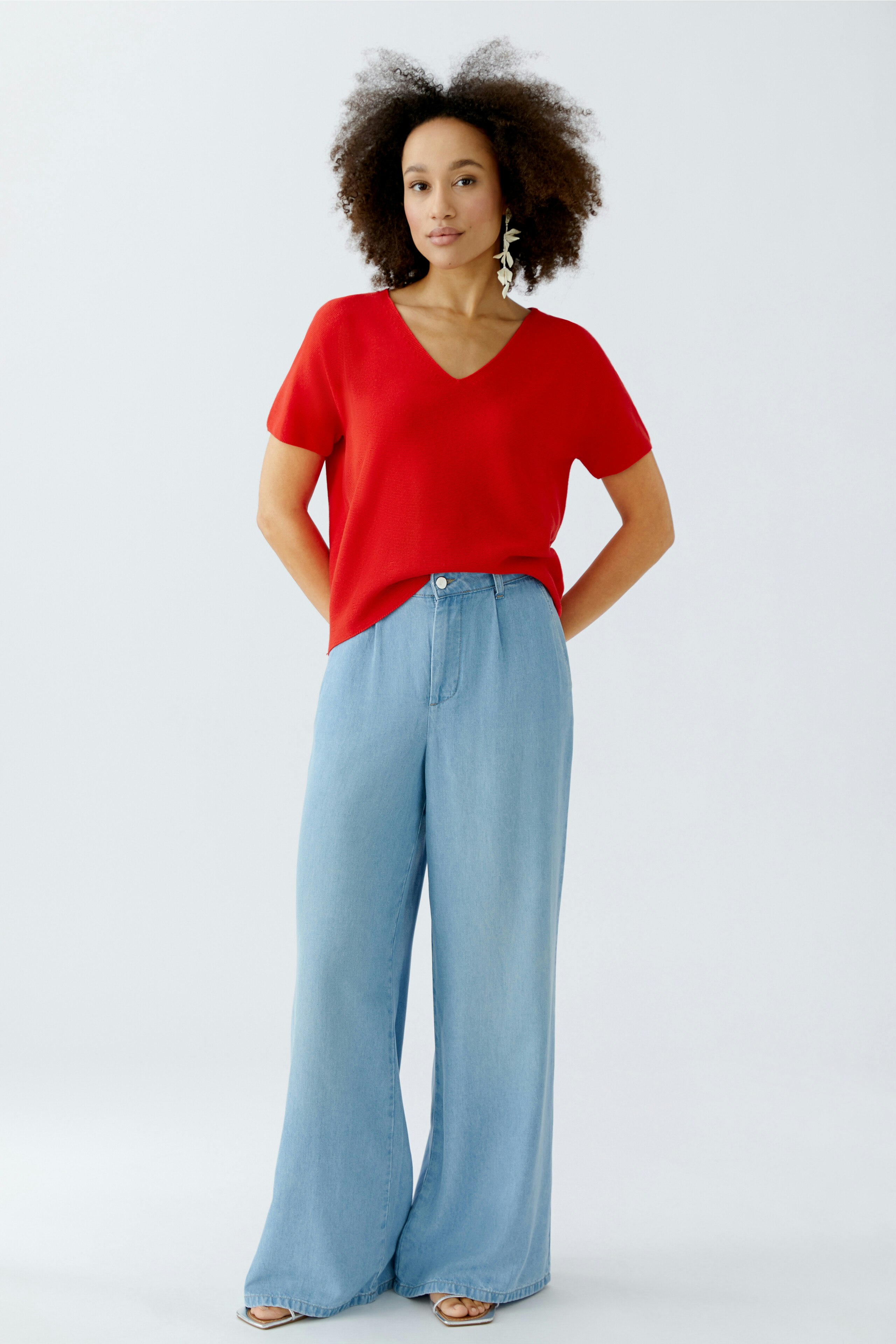 Damen-Pullover: Frau in rotem V-Ausschnitt-Pullover und lässigen Jeans steht entspannt.