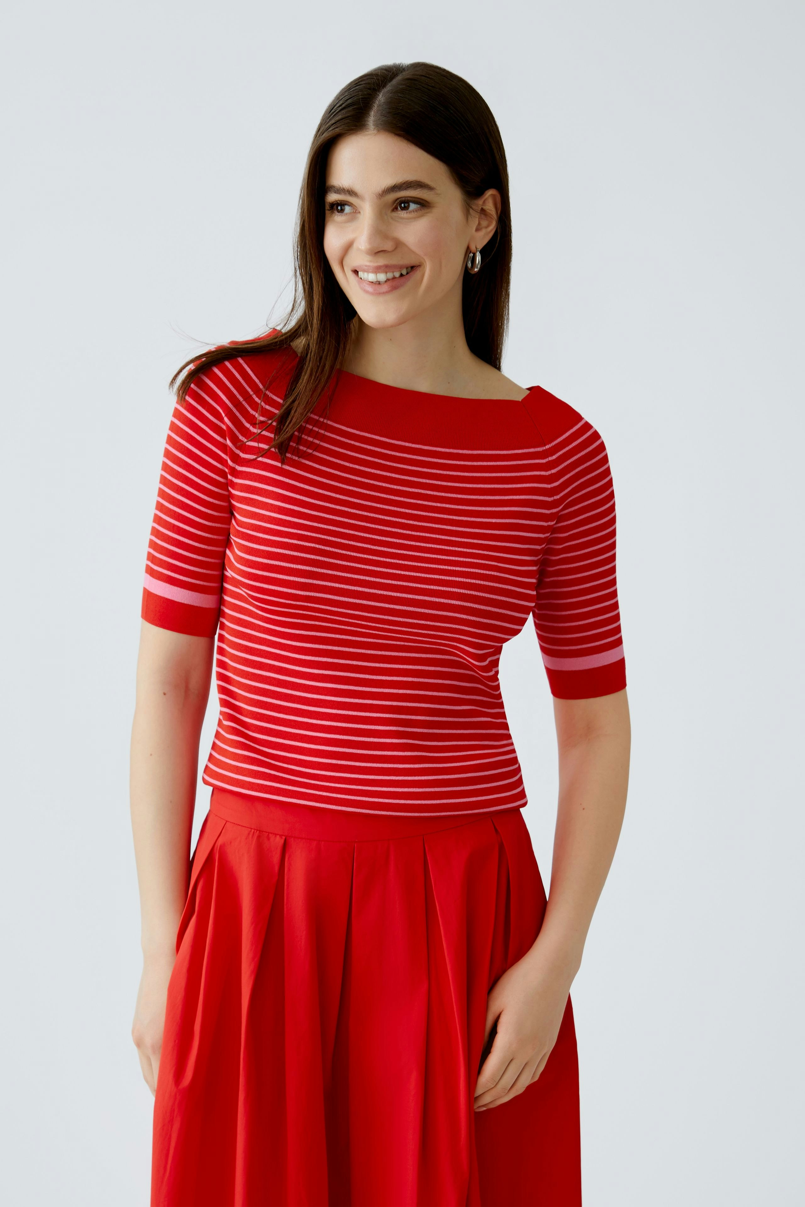Damen-Pullover: Frau in rot-gestreiftem Pullover mit weitem Ausschnitt und lässigem Rock lächelt.