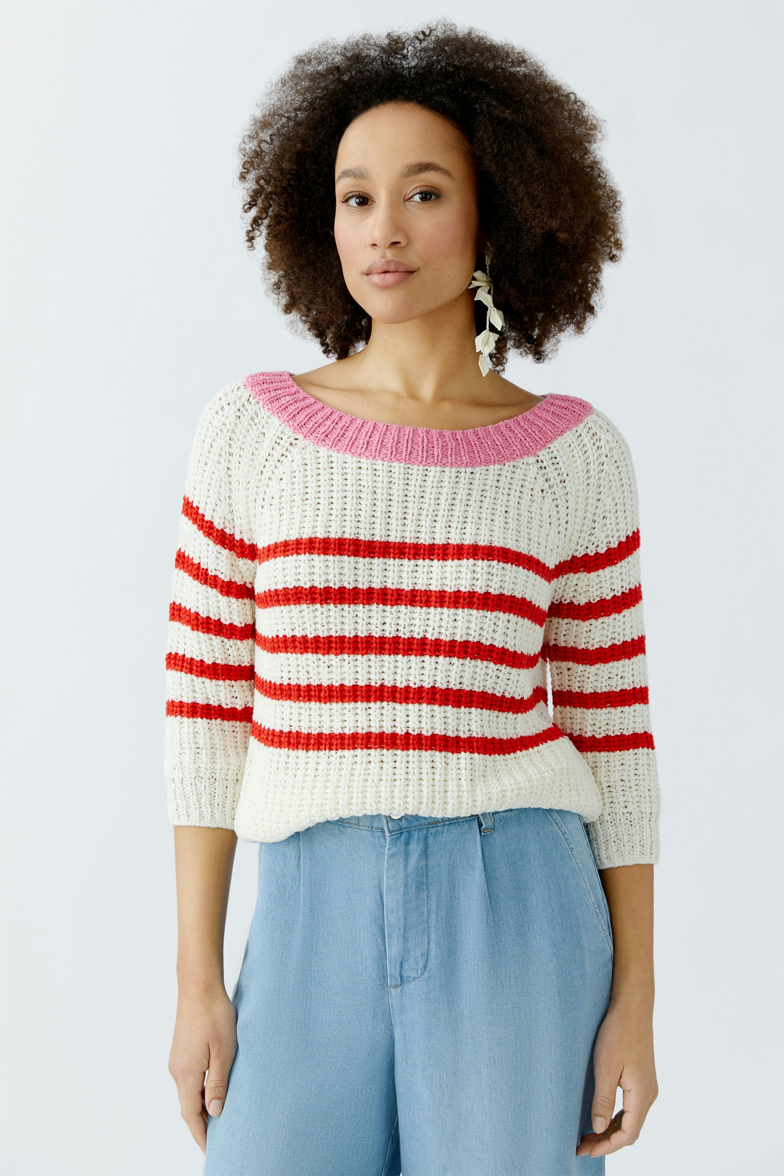 Casual women's pullover: A woman in a striped knit pullover with pink and red stripes, paired with light blue pants.