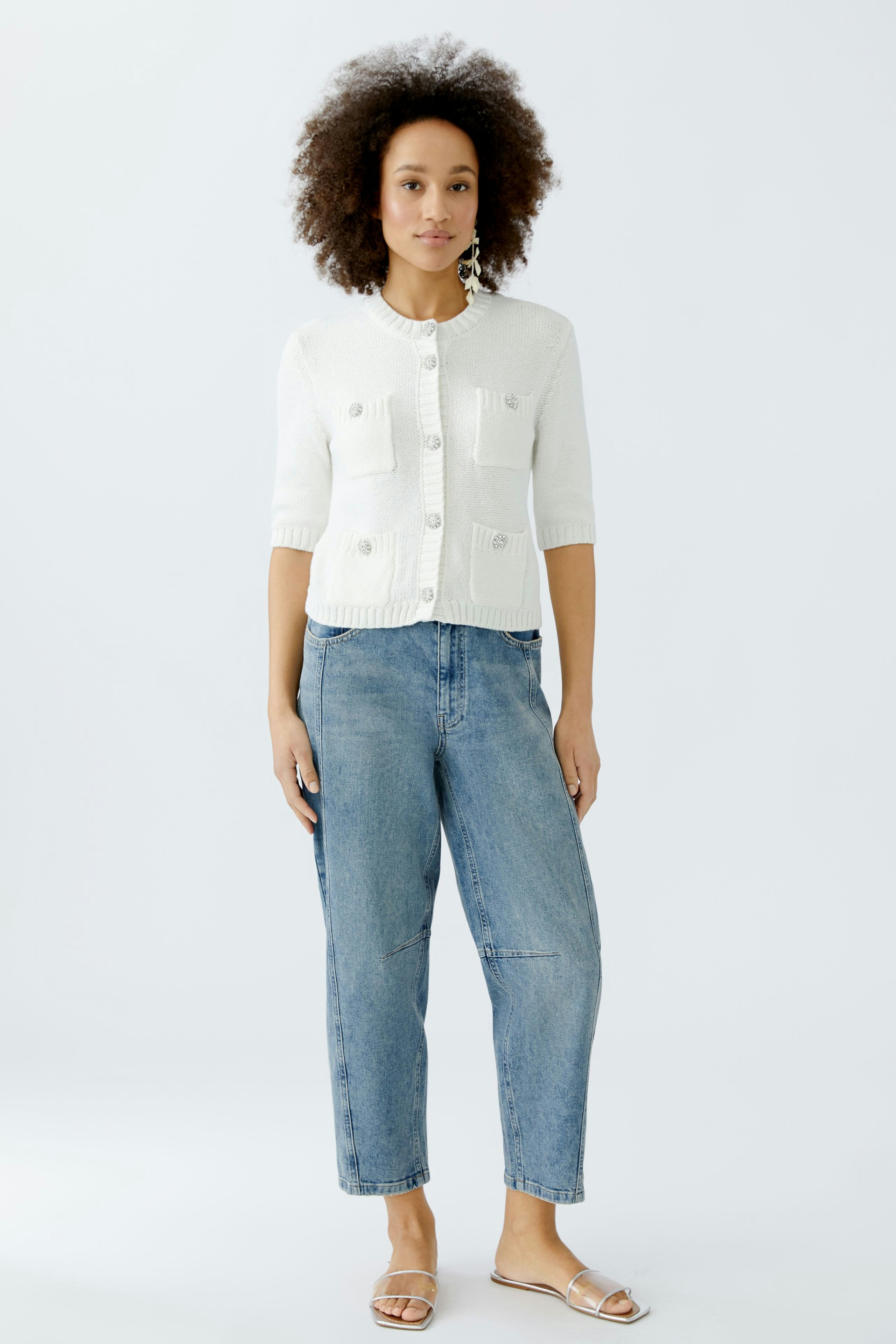 Casual women's cardigan: A woman in a white knitted cardigan with buttons and relaxed-fit jeans.