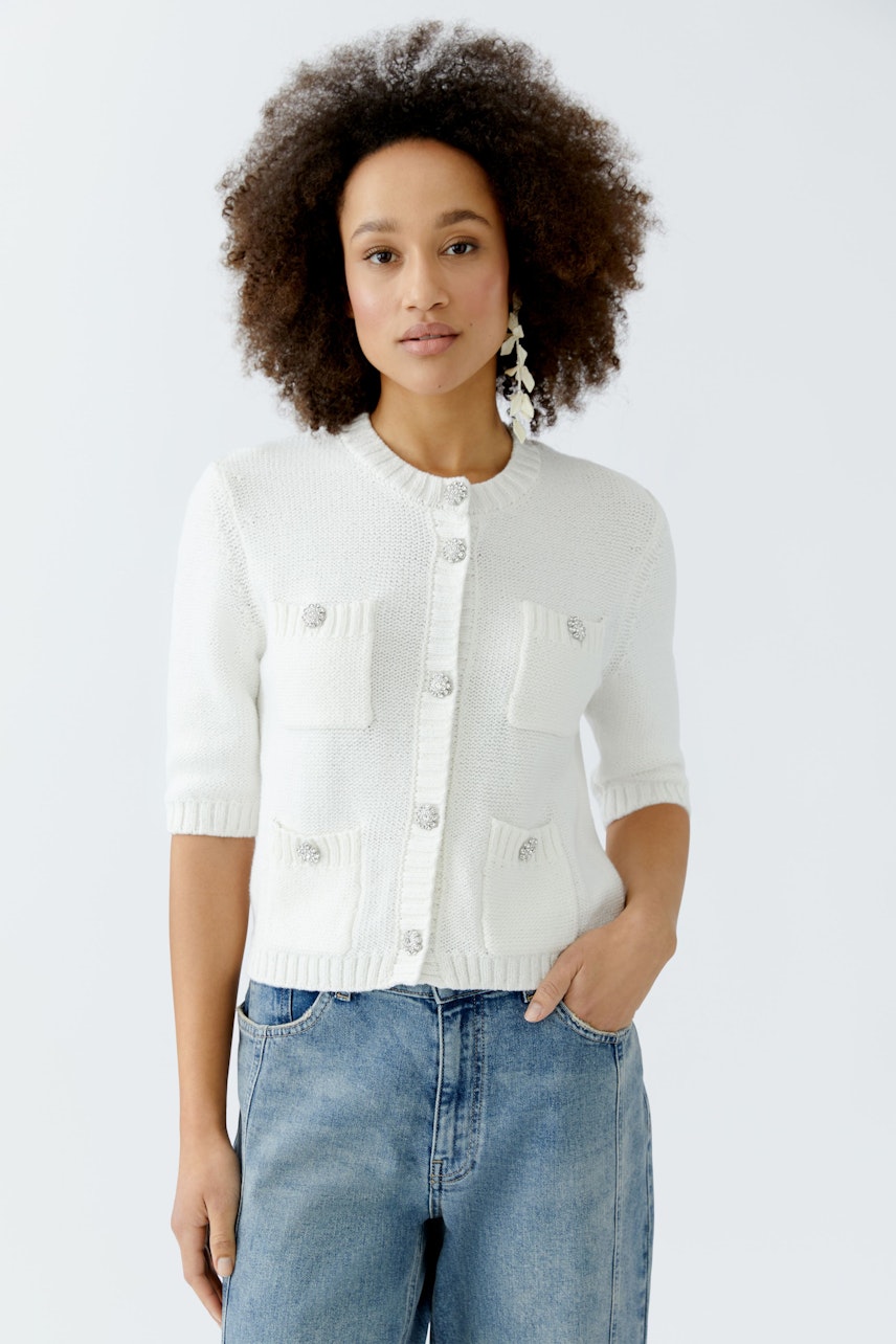 Damen-Strickjacke: Frau in weißer Strickjacke mit Taschen und kurzen Ärmeln, kombiniert mit Jeans.