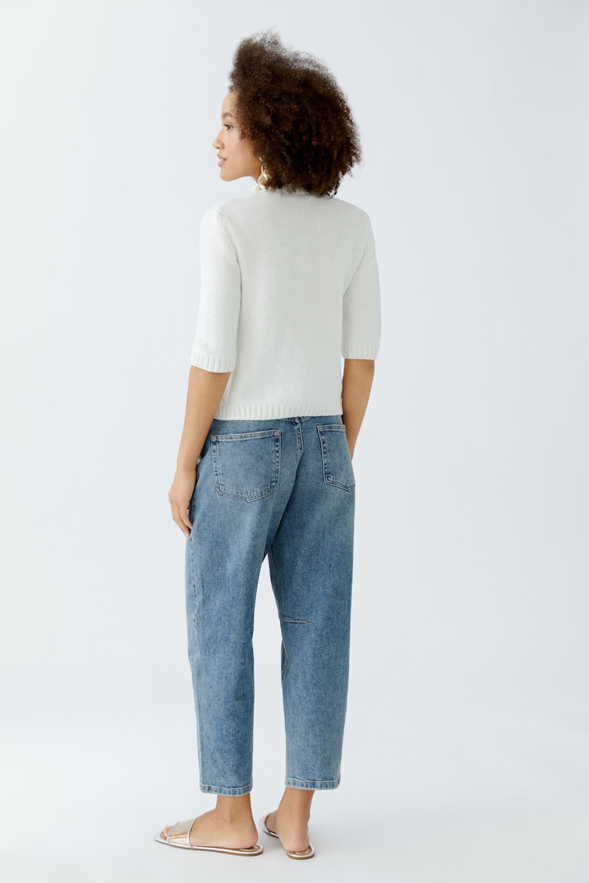 Damen-Strickjacke: Frau mit lockigen Haaren trägt eine helle Strickjacke und lässige Jeans.