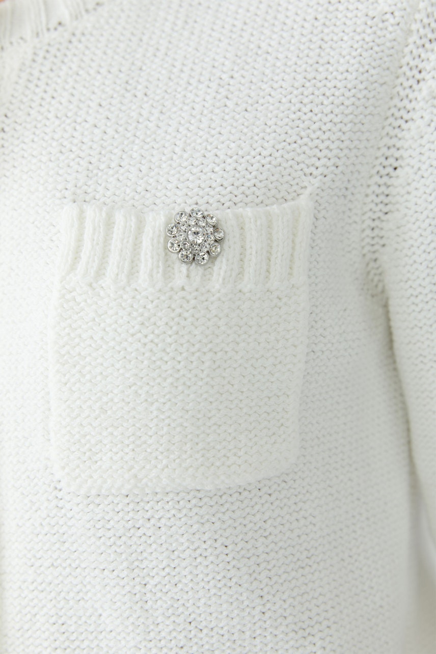 Helle Damen-Strickjacke mit einer dekorativen Blume auf der Brusttasche.