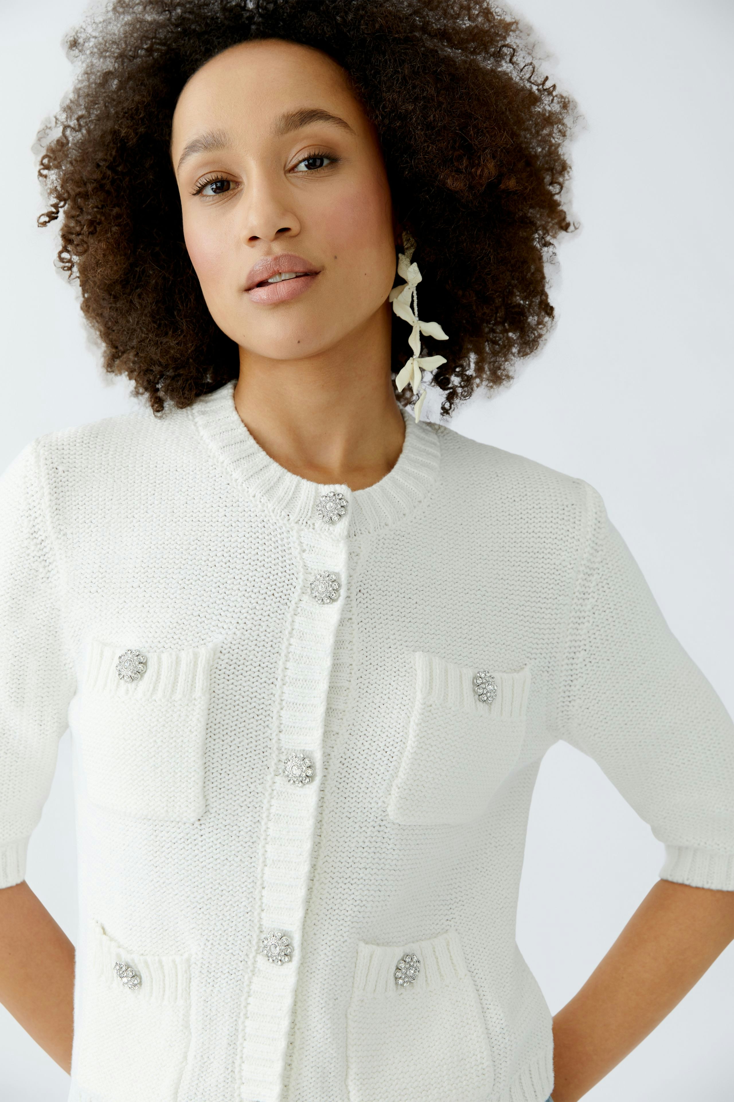 Casual women's cardigan: Young woman in a white knitted cardigan with pockets and buttons, smiling confidently.