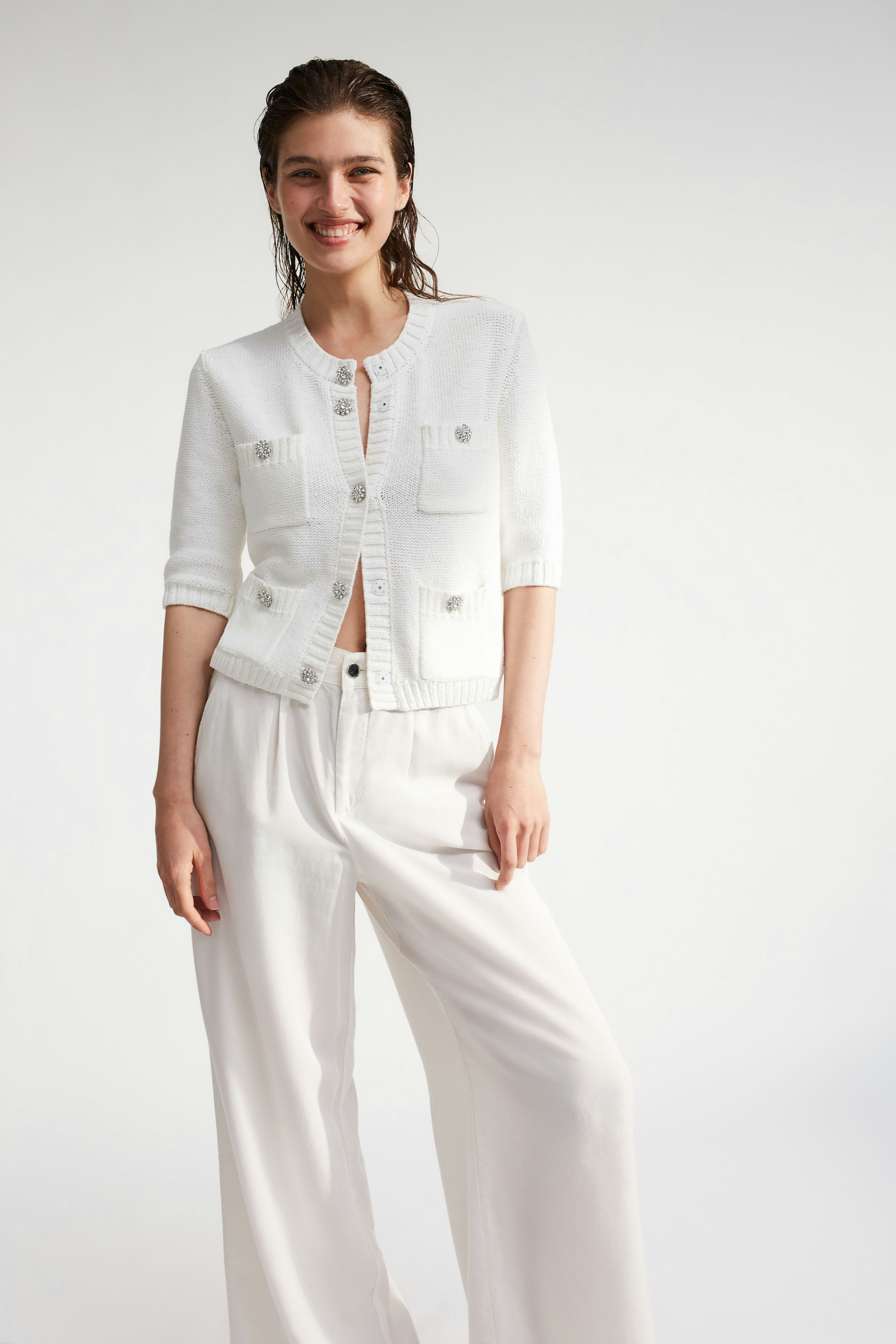 Casual women's cardigan: A woman in a white cardigan with pockets and buttons, paired with wide trousers.