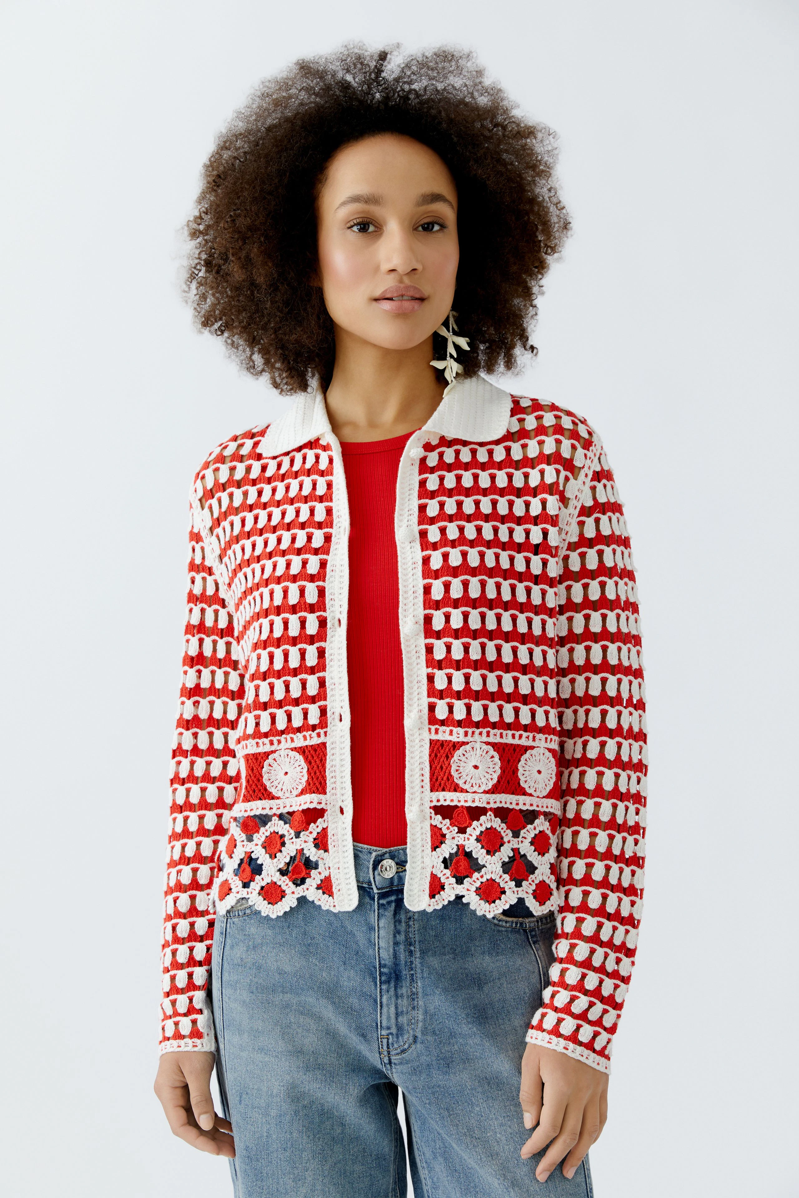 Bunte Damen-Strickjacke: Frau trägt eine rote Strickjacke mit weißen Mustern und lässigen Jeans.