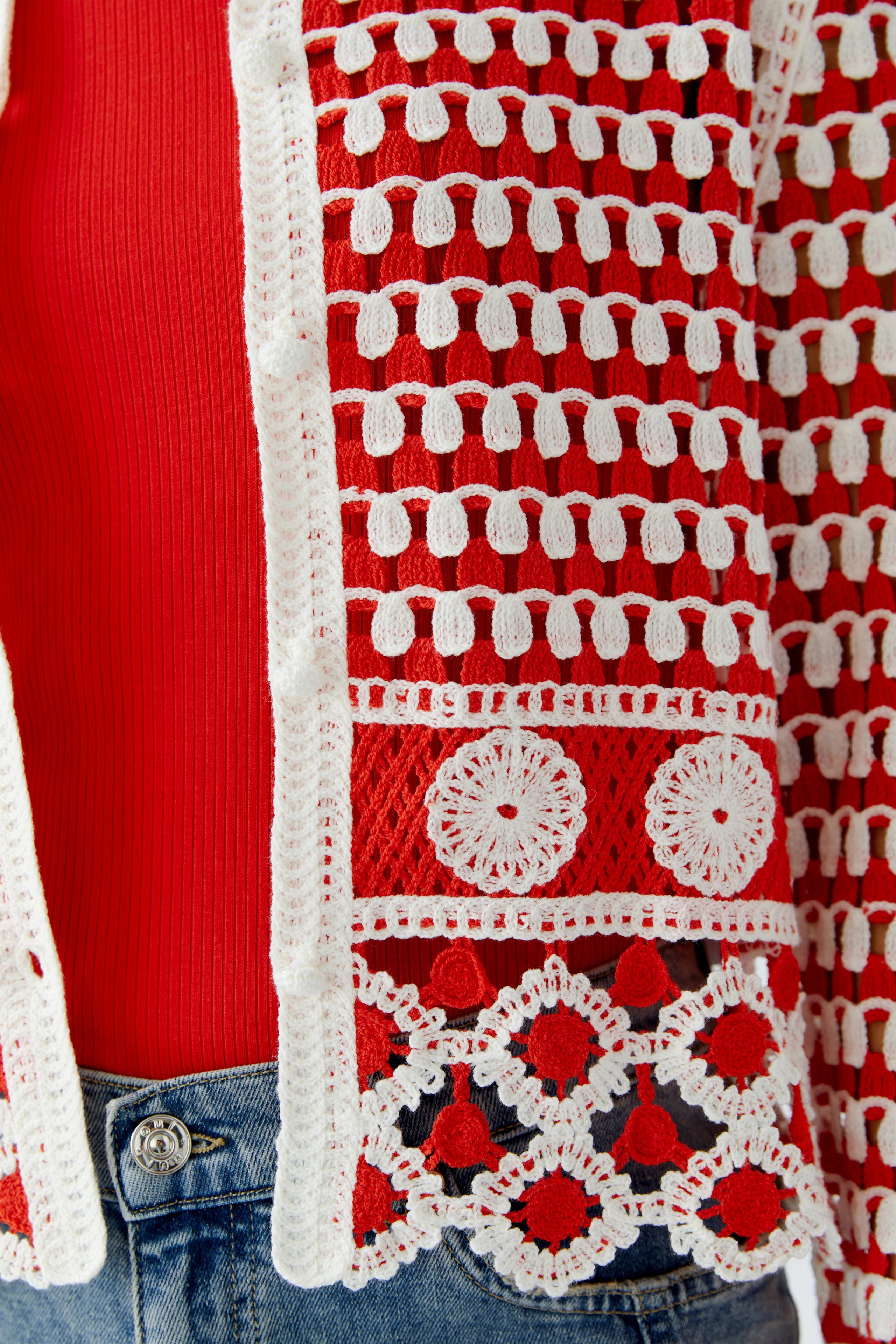 Helle Damen-Strickjacke in Rot mit weißen Details, lässig über einem roten Top getragen.