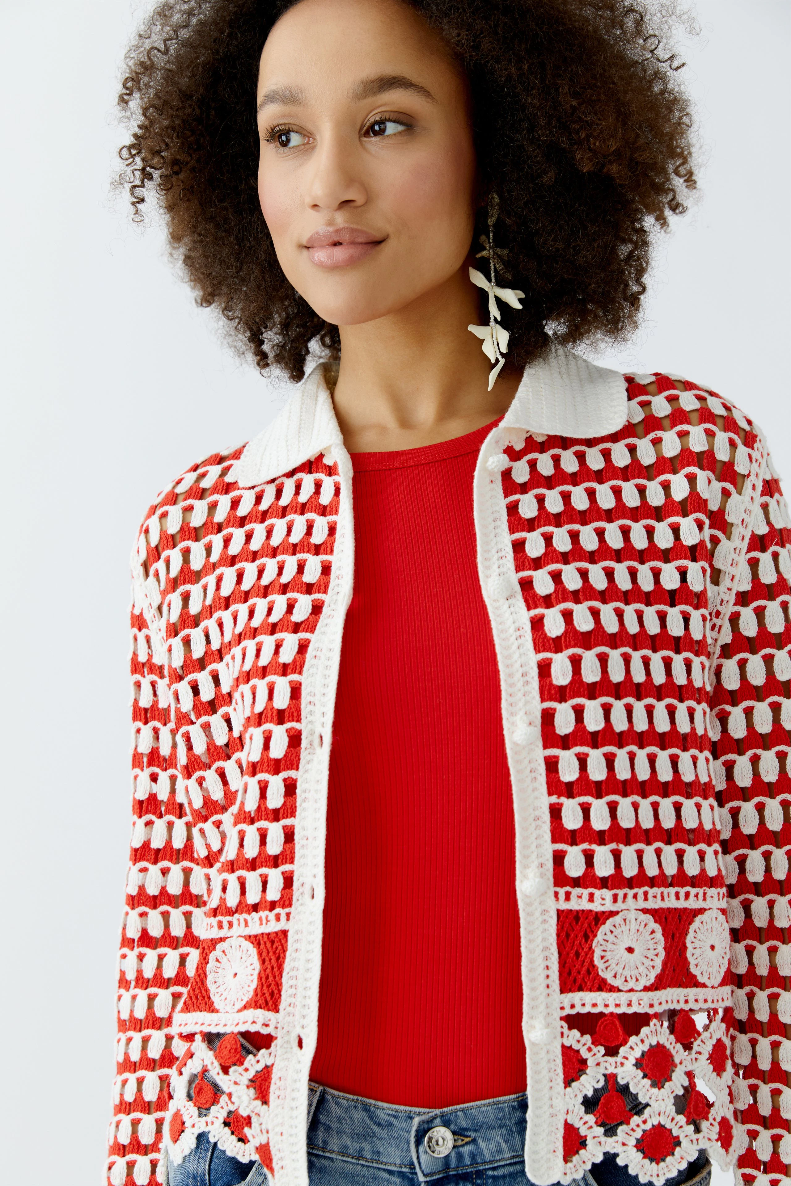 Helle Damen-Strickjacke mit buntem Muster, kombiniert mit rotem Oberteil und lässigen Jeans.